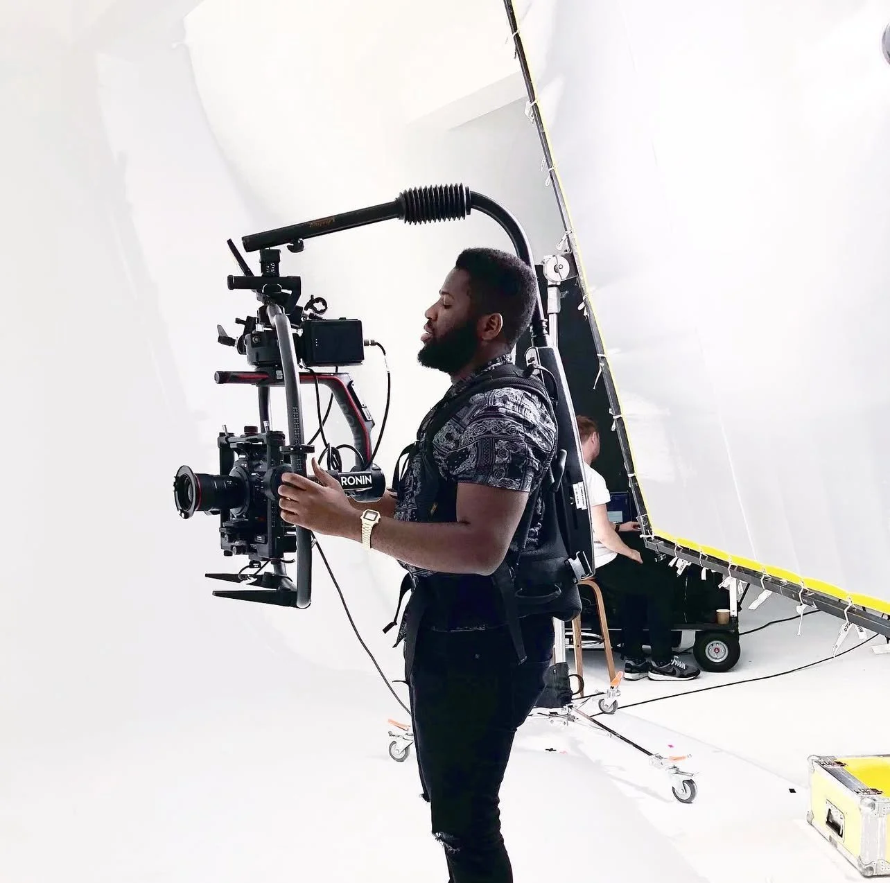 A man operating a professional video camera on a film set in Dubai with white background and equipment.