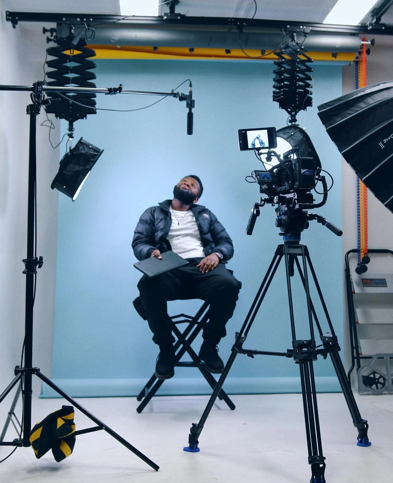 Man sitting in front of camera on a film set or video shoot in Dubai with lighting and equipment, blue backdrop, and recording gear.