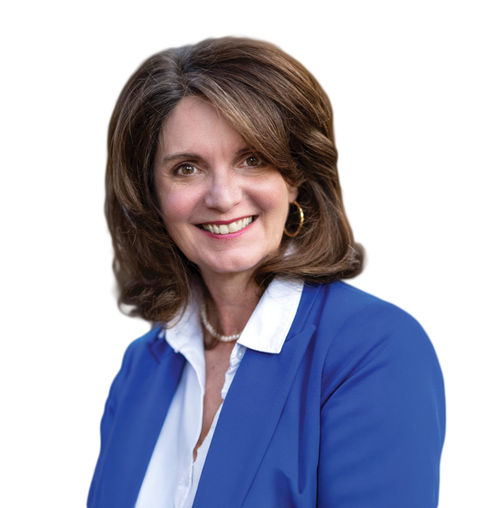 A woman with brown hair smiling, wearing a blue blazer over a white shirt and a pearl necklace, with a blurred outdoor background.