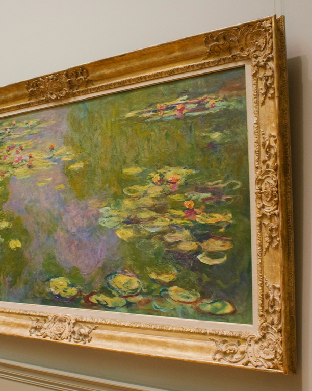 A framed Impressionist-style painting of a pond with water lilies, featuring green, yellow, pink, and purple colors, signed 'Claude Monet 19'.