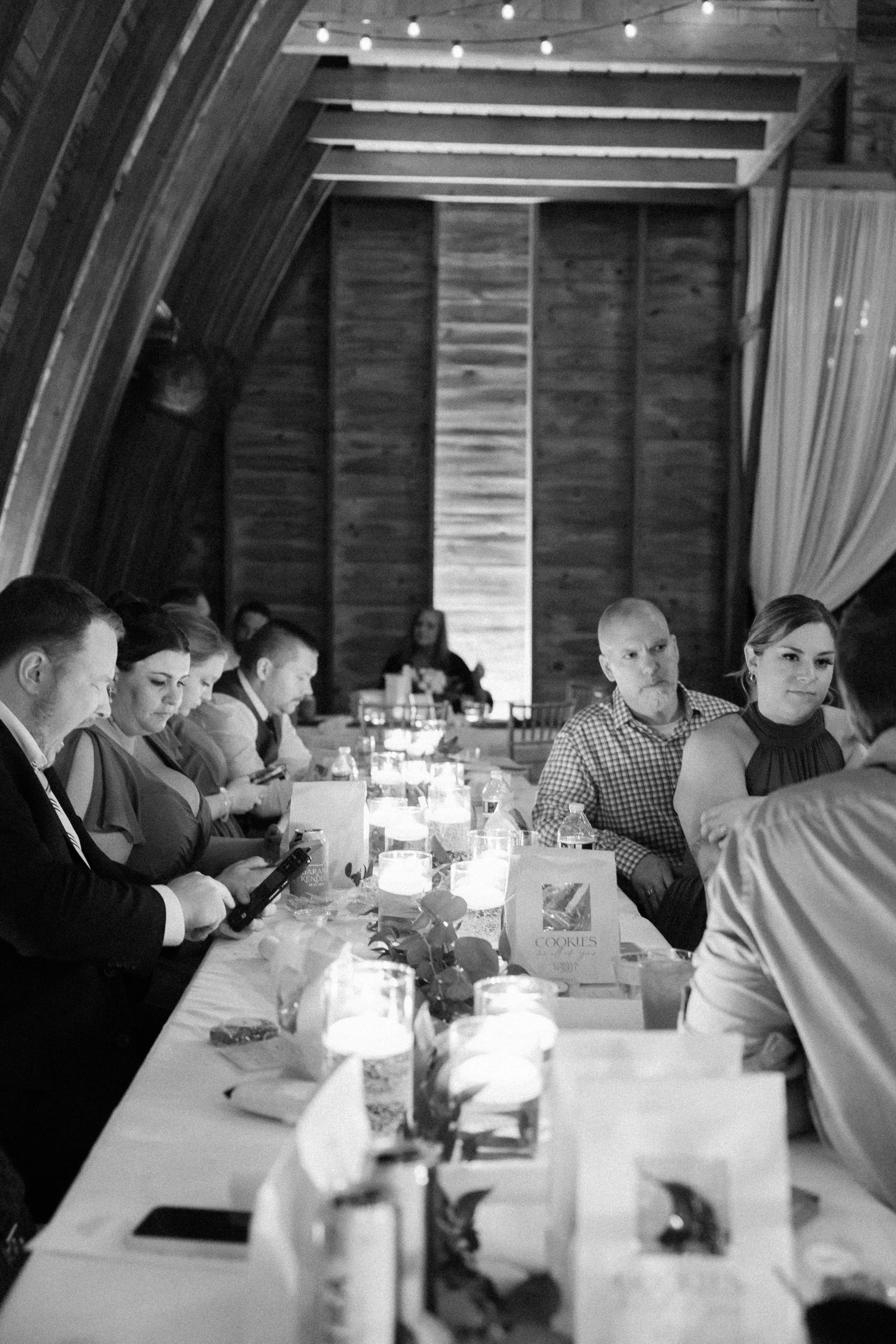 People sitting at a long banquet table during a formal event, with candles and decorations, in a wooden hall.