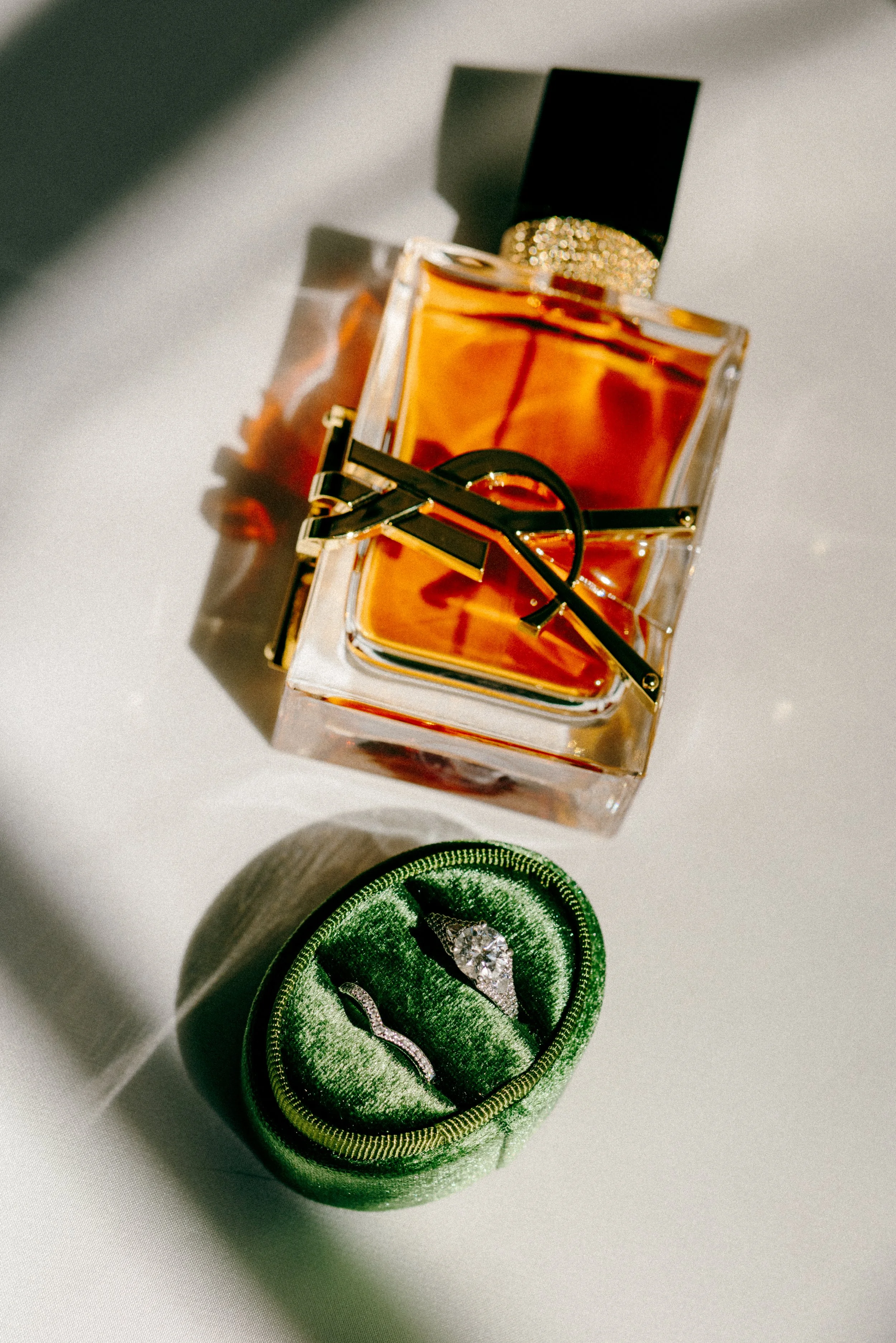 A bottle of perfume and jewelry in a green velvet ring box