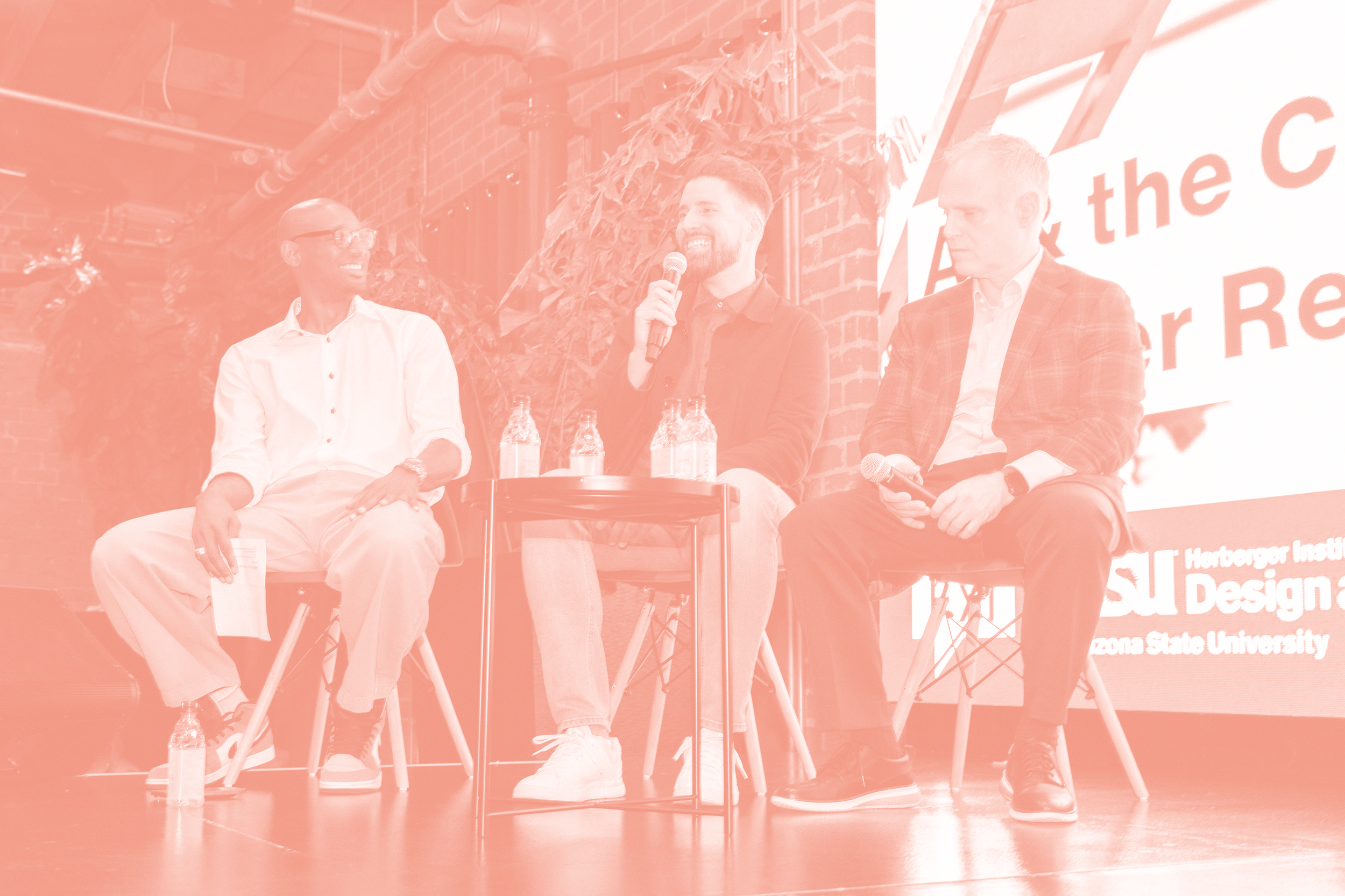Three men sitting on chairs in a panel discussion, with two holding microphones.