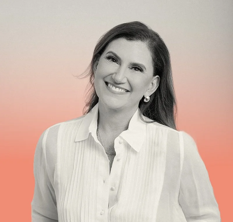A smiling woman with shoulder-length hair, wearing a white collared shirt and pearl earrings, against a gradient background from pink to beige.