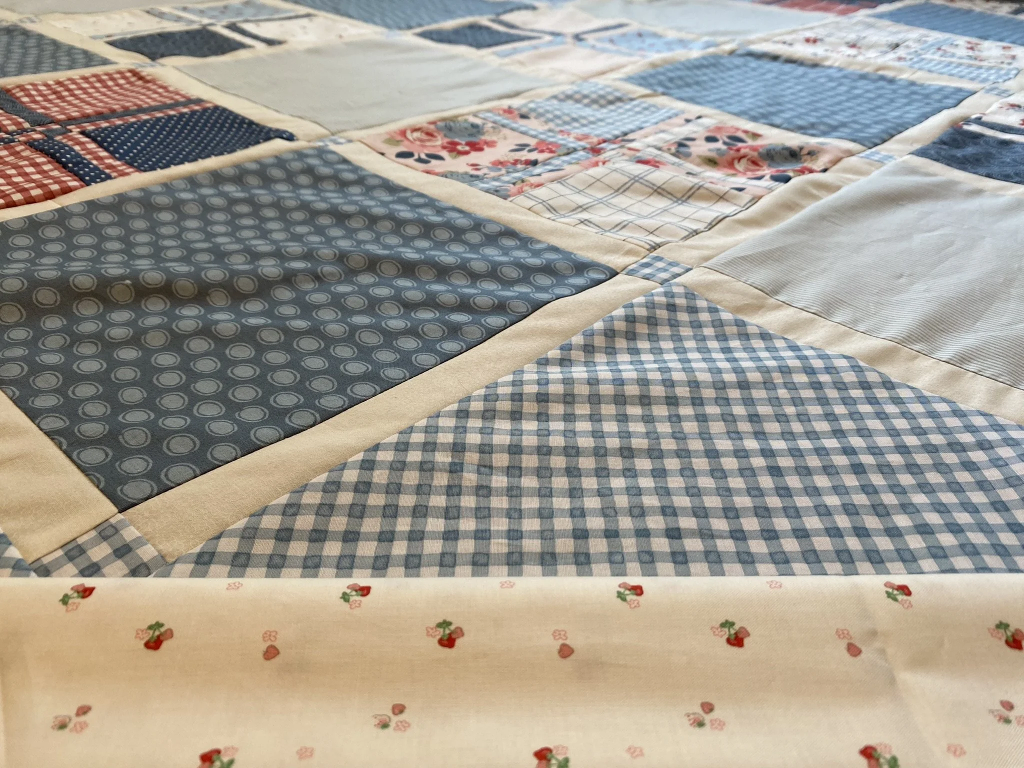Close-up of a patchwork quilt with various blue, red, and white patterned fabrics, including polka dots, checks, and floral designs.