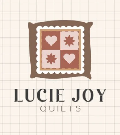 Lucie Joy Quilts logo featuring a square quilt with four patches of hearts and star-like shapes, surrounded by a brown frame, on graph paper background.