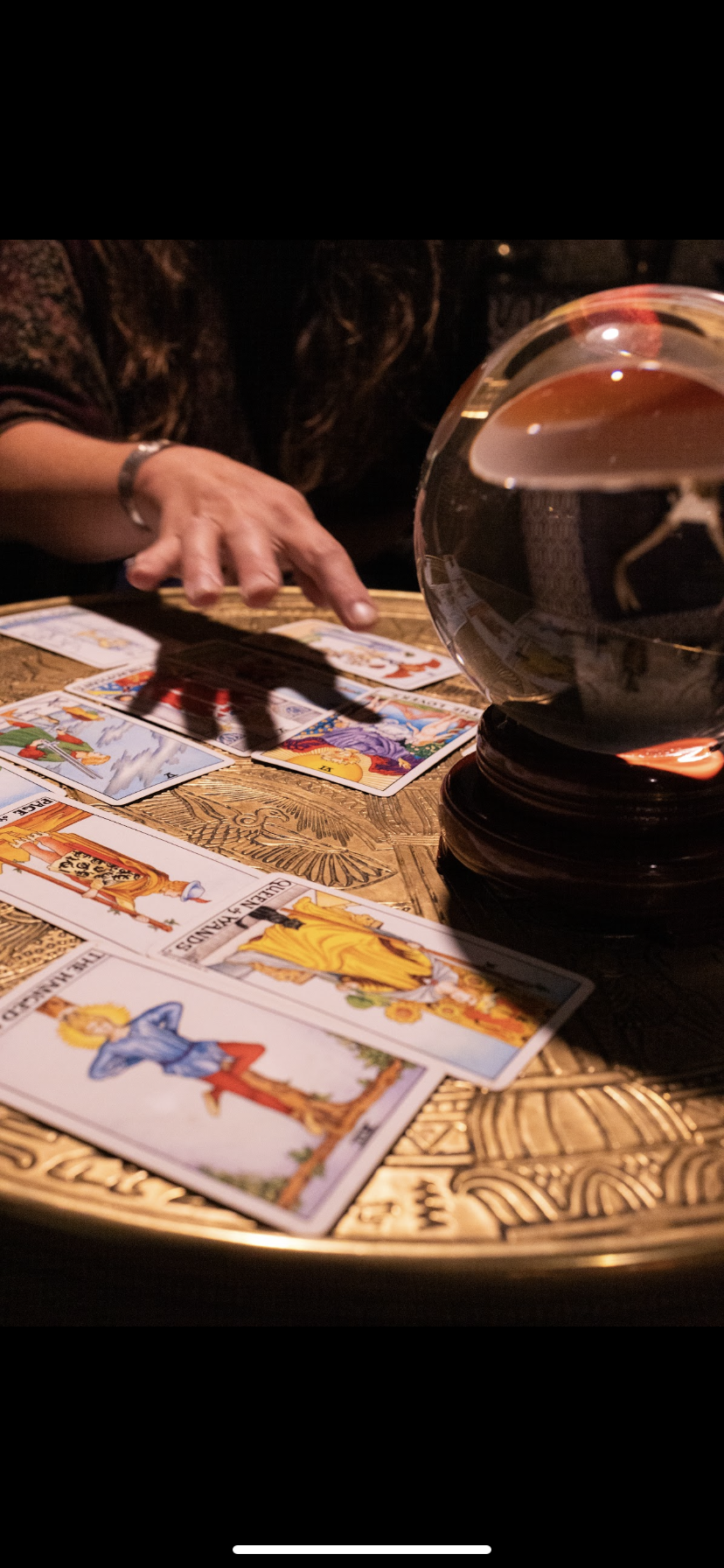 Person performing a tarot card reading with tarot cards spread on aDecorative wooden table, a large glass of red wine nearby.