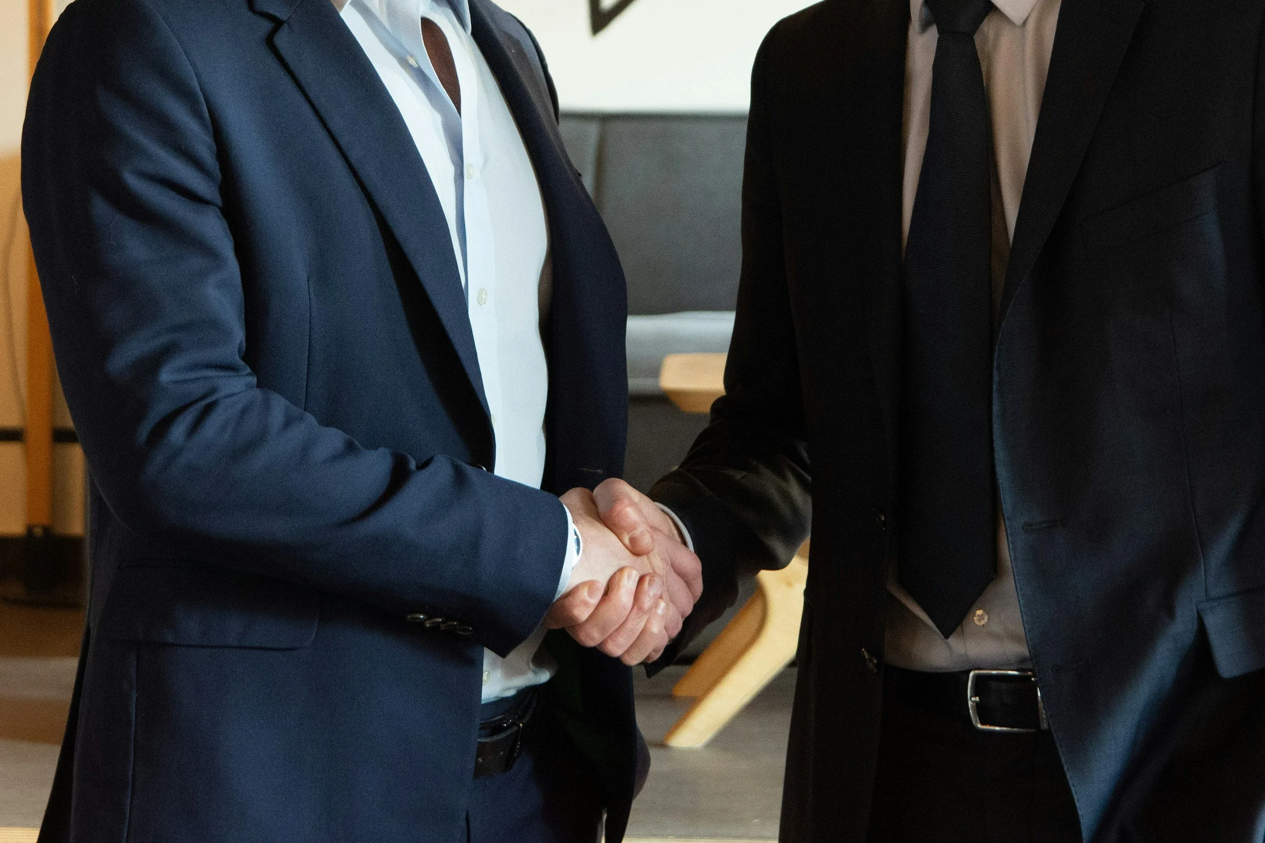 Two men in business suits shaking hands indoors.