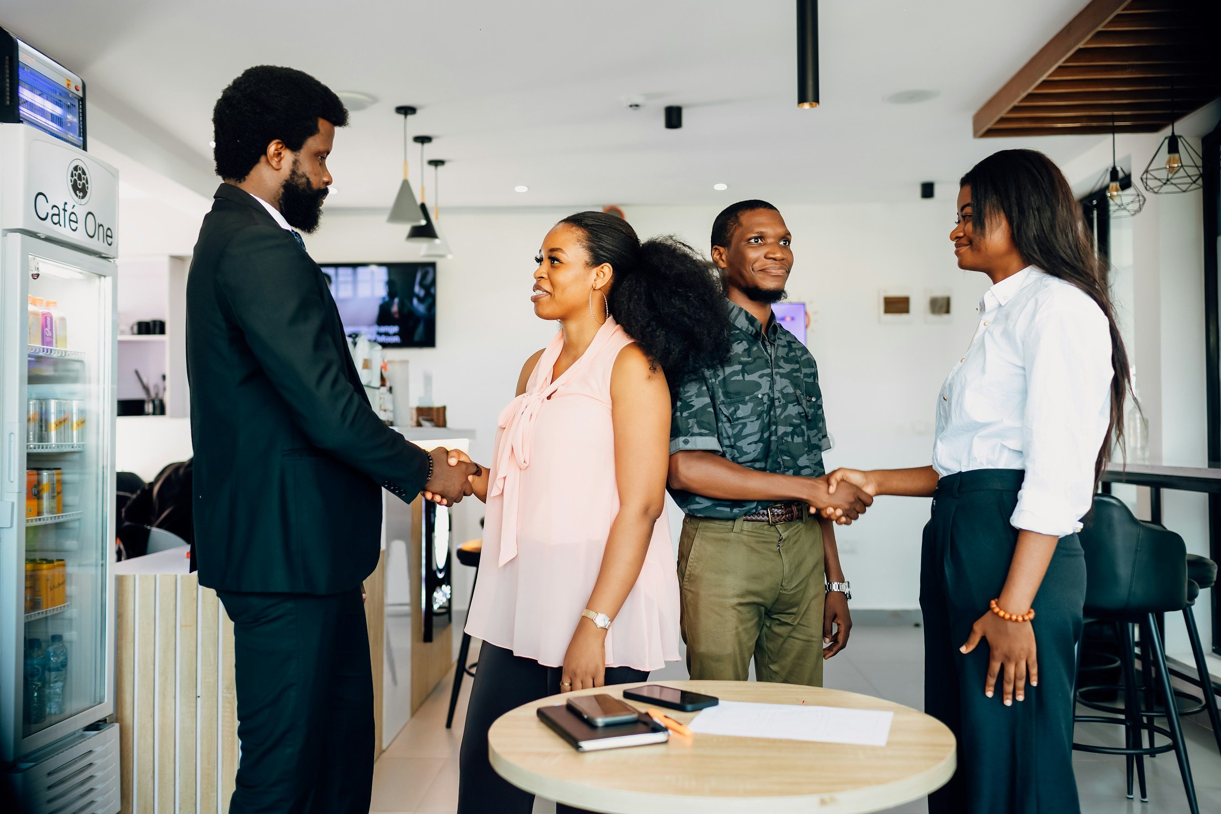 Two men and two women shaking hands and exchanging smiles in a coffee shop.