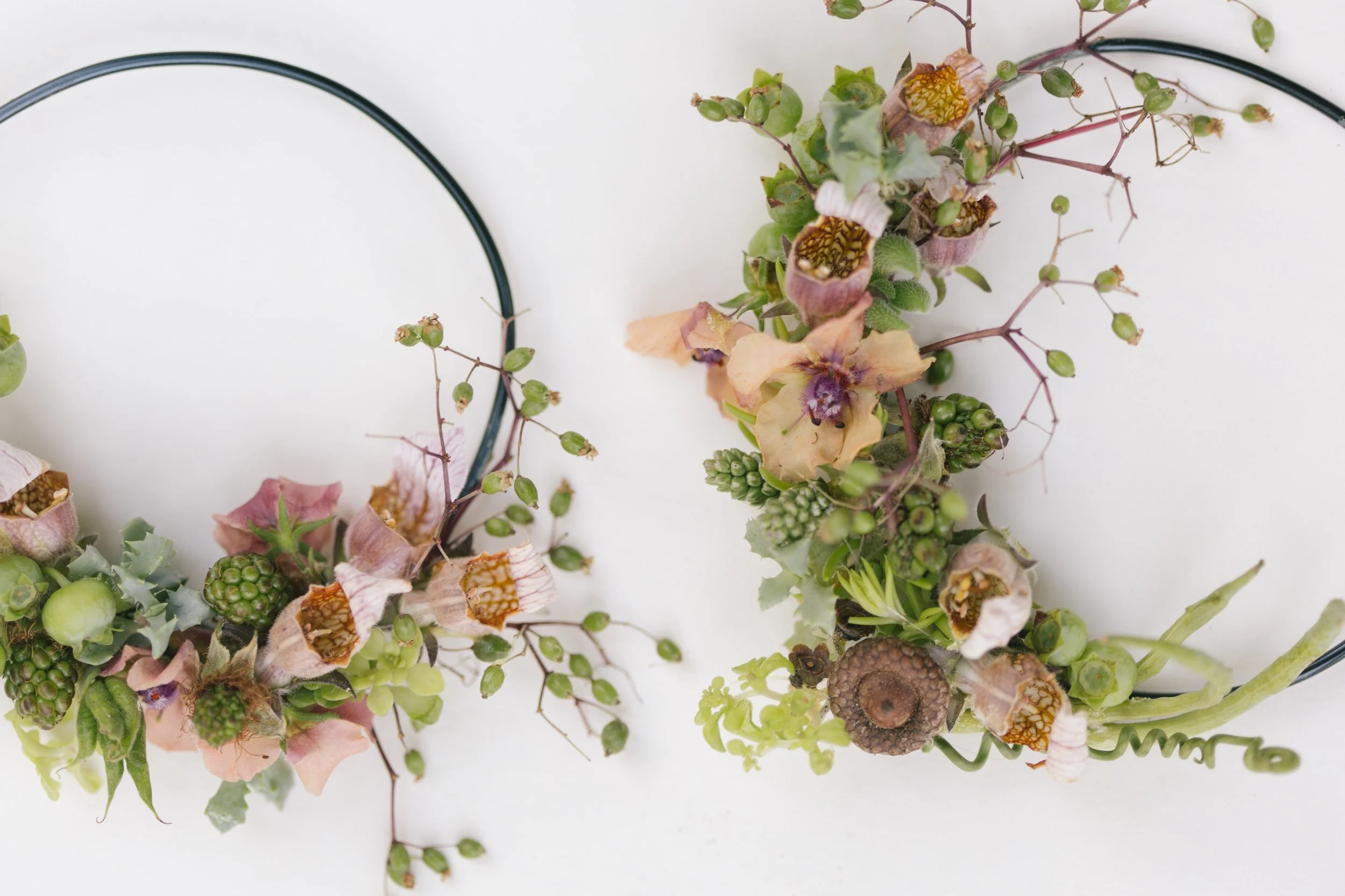 Floral hoop earings with pink and brown flowers, green berries, and foliage on a white background.