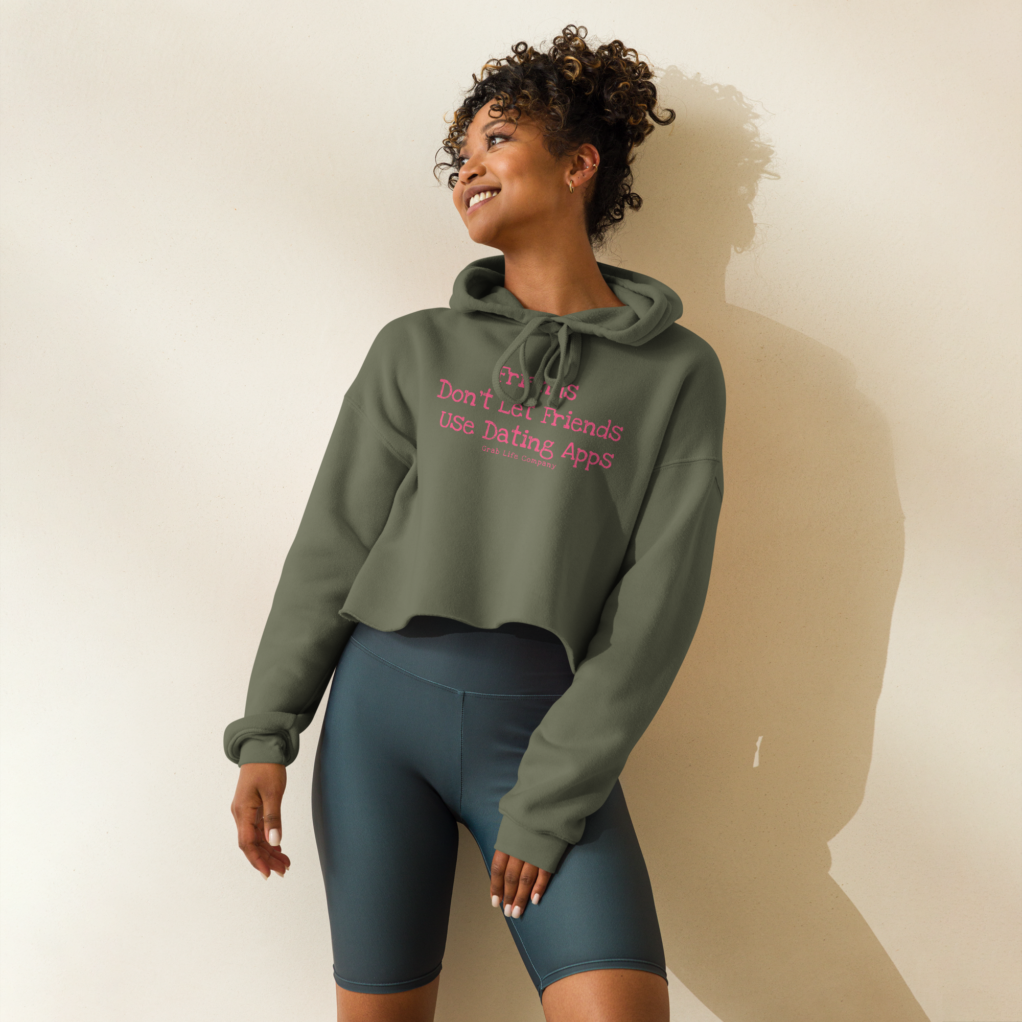 Grab Life Company cropped hoodie with Friends don't let Friends use Dating Apps printed on the front in bright pink on military green sweatshirt.
