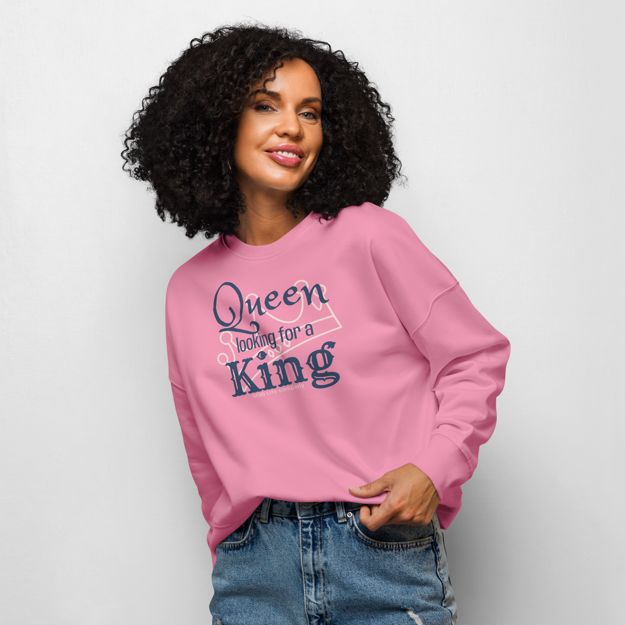 Grab Life Company women's crew neck sweatshirt with Queen Looking for a King printed in navy blue on a bubble pink sweatshirt. Image shows woman wearing the shirt.