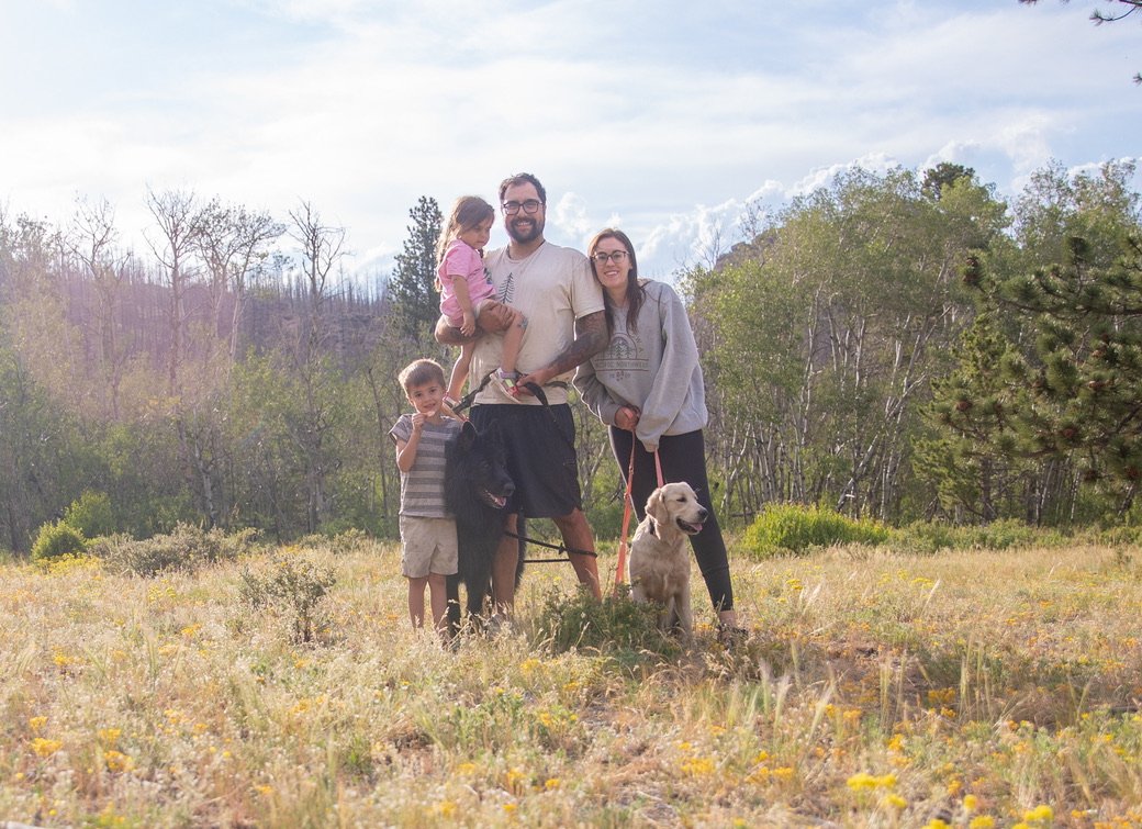 The family who owns Fable Marketing Co with dogs standing outdoors in Colorado a field with trees in the background.