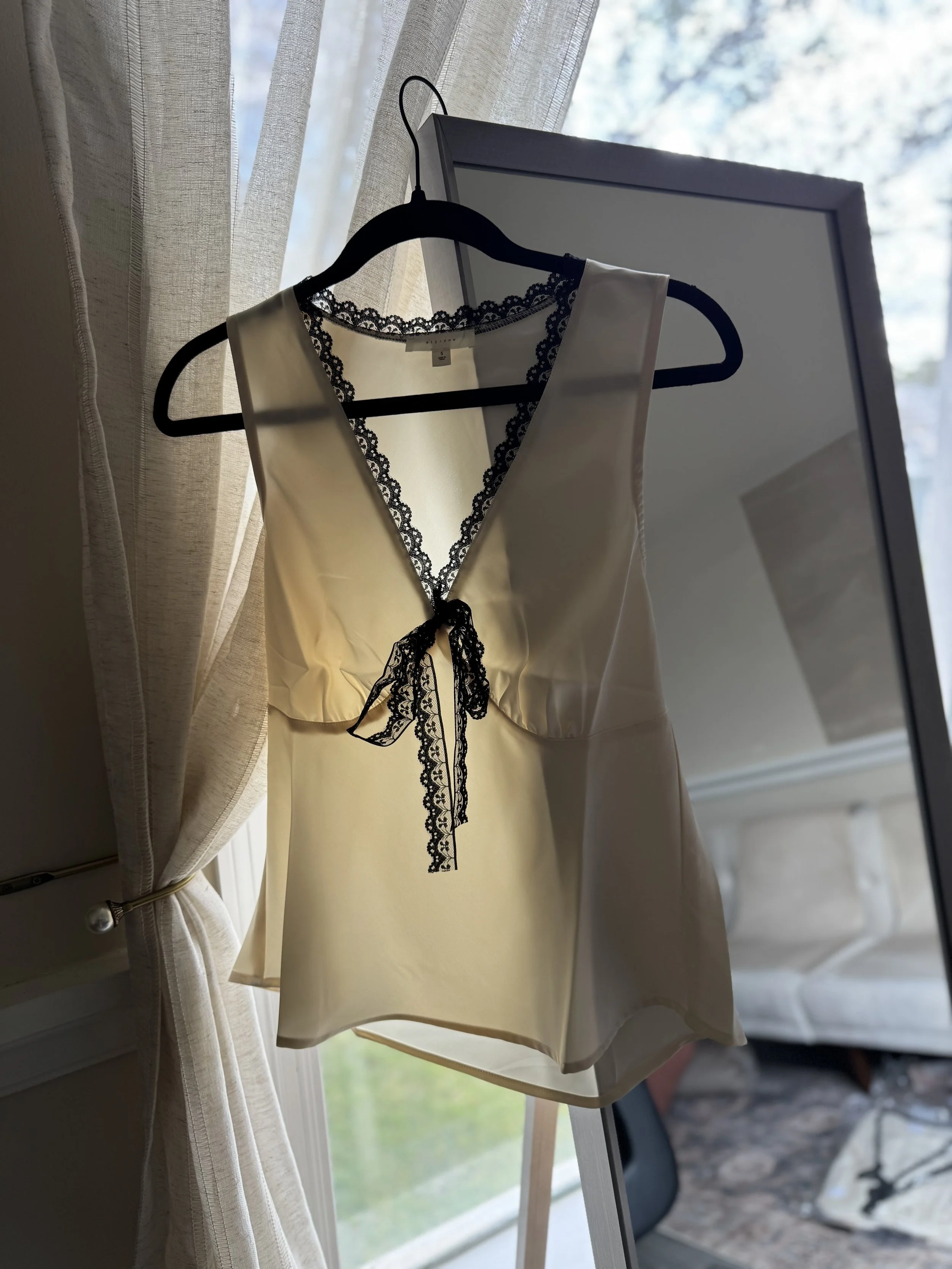 Sleeveless cream top with contrast trim and front tie detail.