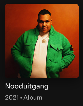 A man wearing a green jacket and a white shirt, posing against an orange background, with an album cover titled "Nooduitgang" from 2021.