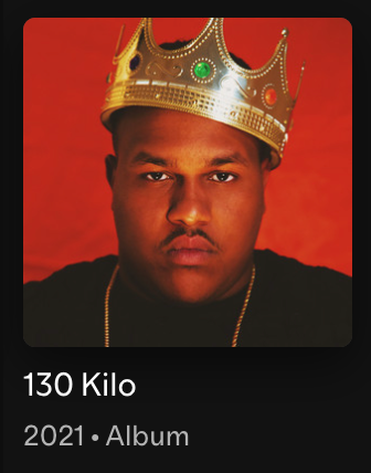 A young man wearing a gold crown with red, green, and white jewels, against a red background.