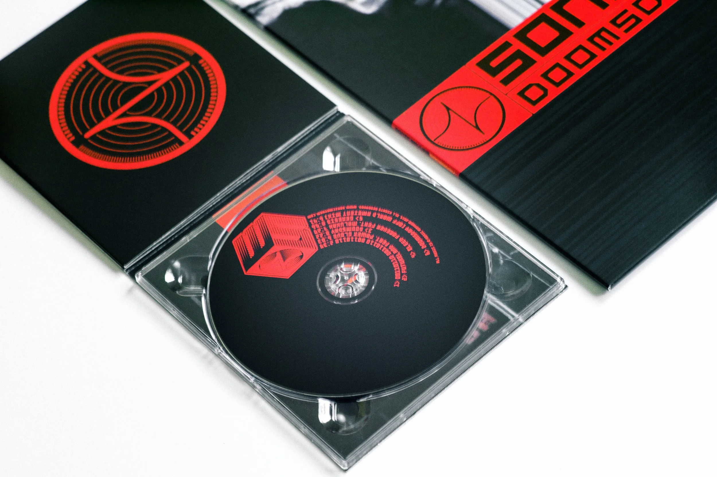 A compact disc in a jewel case, a CD cover with black and red design, and related packaging.