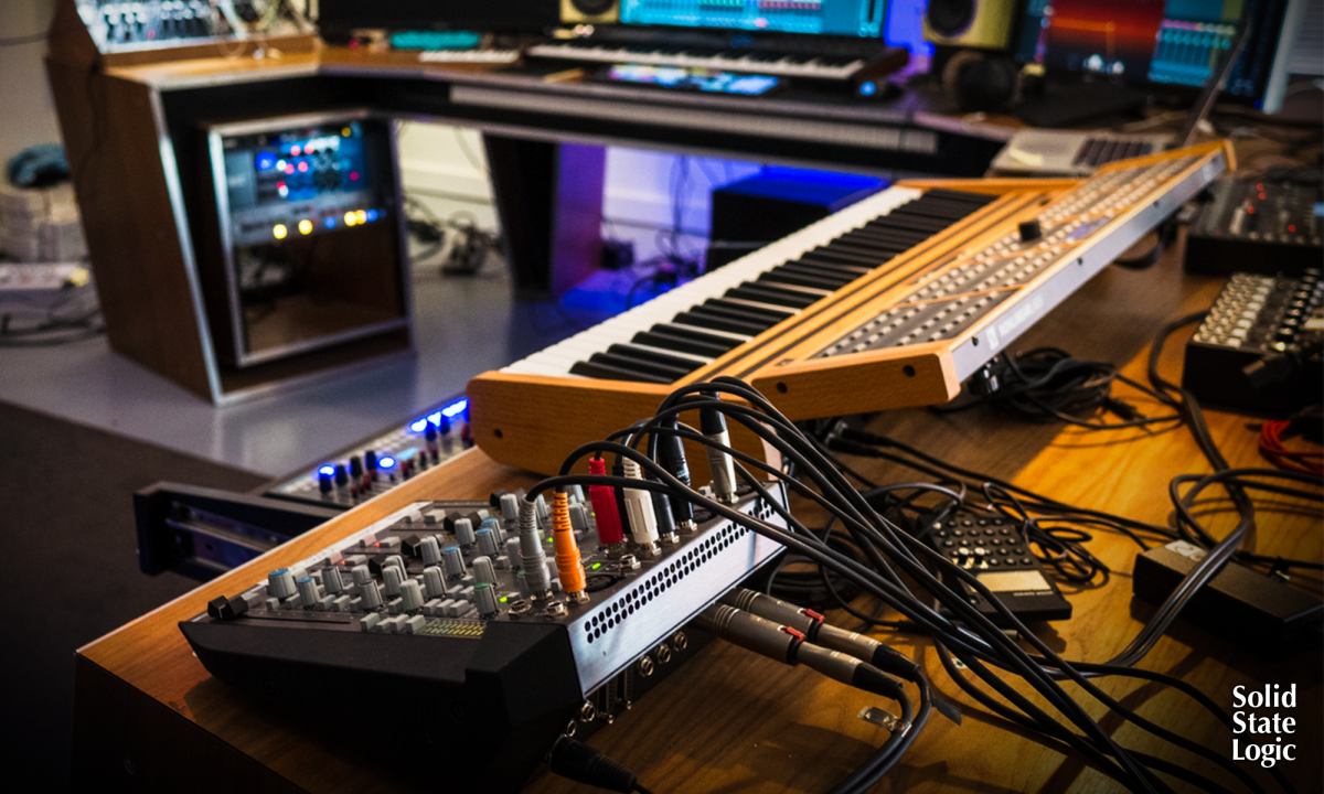 Music studio with synthesizers, mixing console, and audio equipment on a wooden desk.