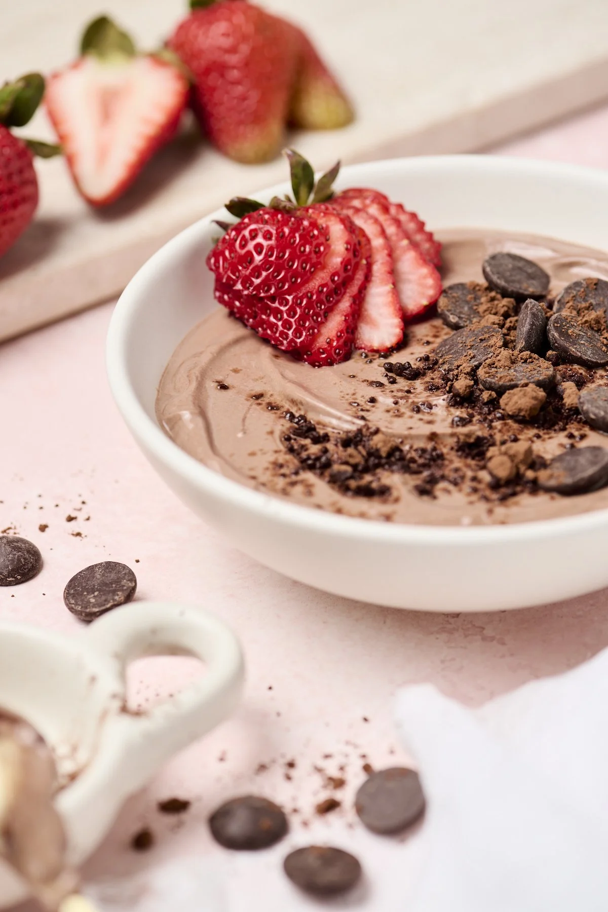 A bowl of brownie batter dip topped with sliced strawberries and chocolate chips, with additional strawberries and chocolate chips scattered nearby.