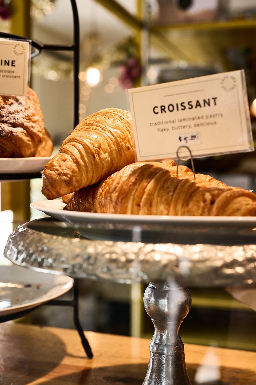 Fresh croissants on display with a sign indicating their price, in a bakery setting.