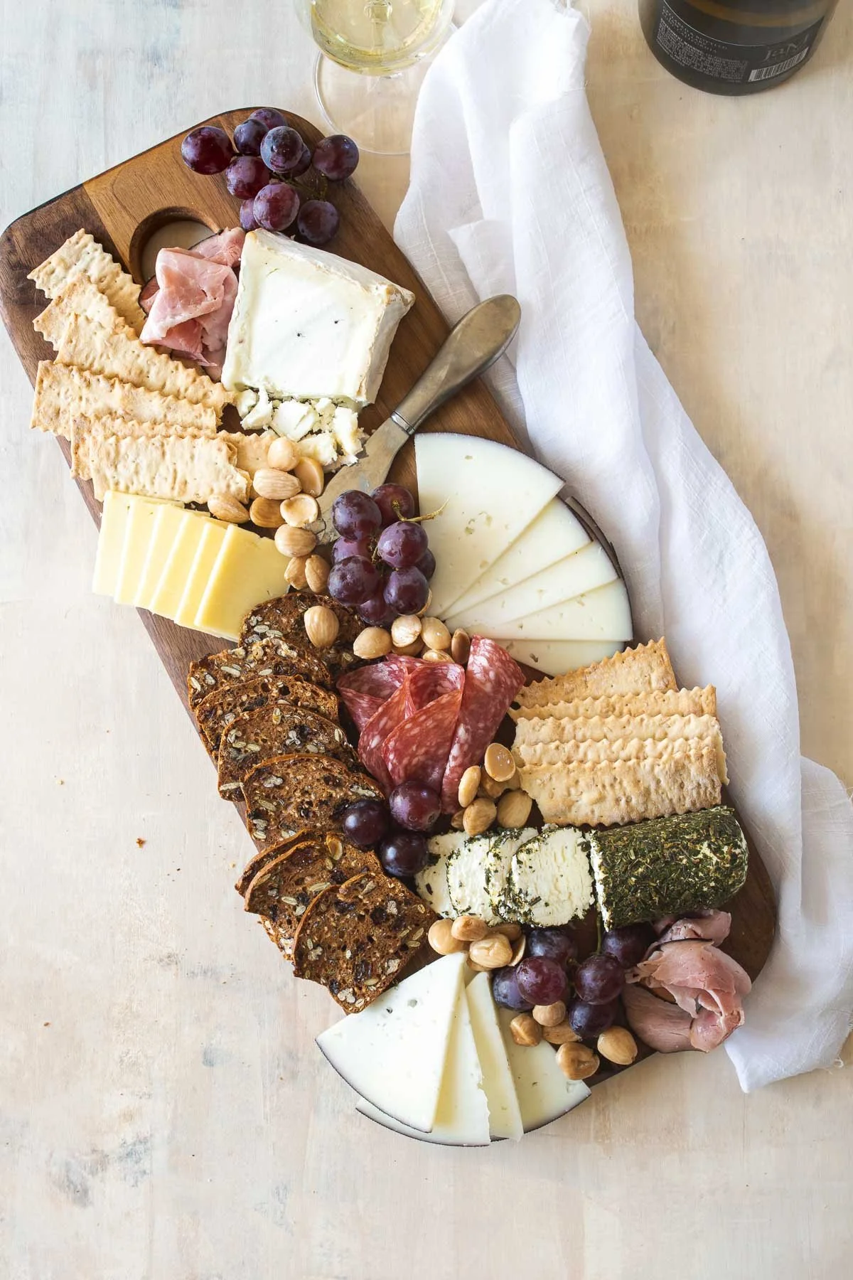 Charcuterie board with various cheeses, cured meats, grapes, nuts, crackers, and fruit on a wooden platter.