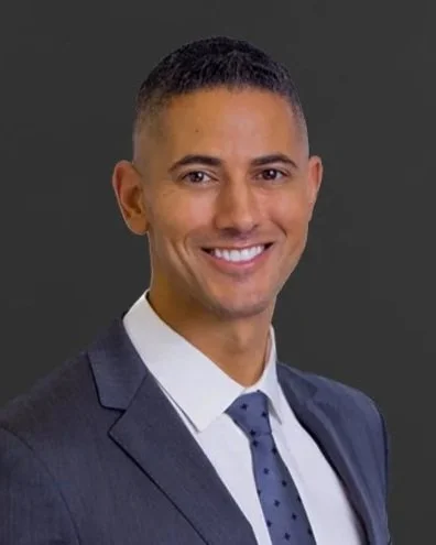 Professional man in a suit smiling against a gray background.