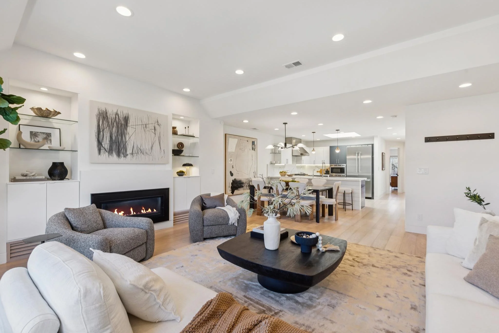 Open-concept living room with white walls, modern furniture, a fireplace, and a view into the kitchen.