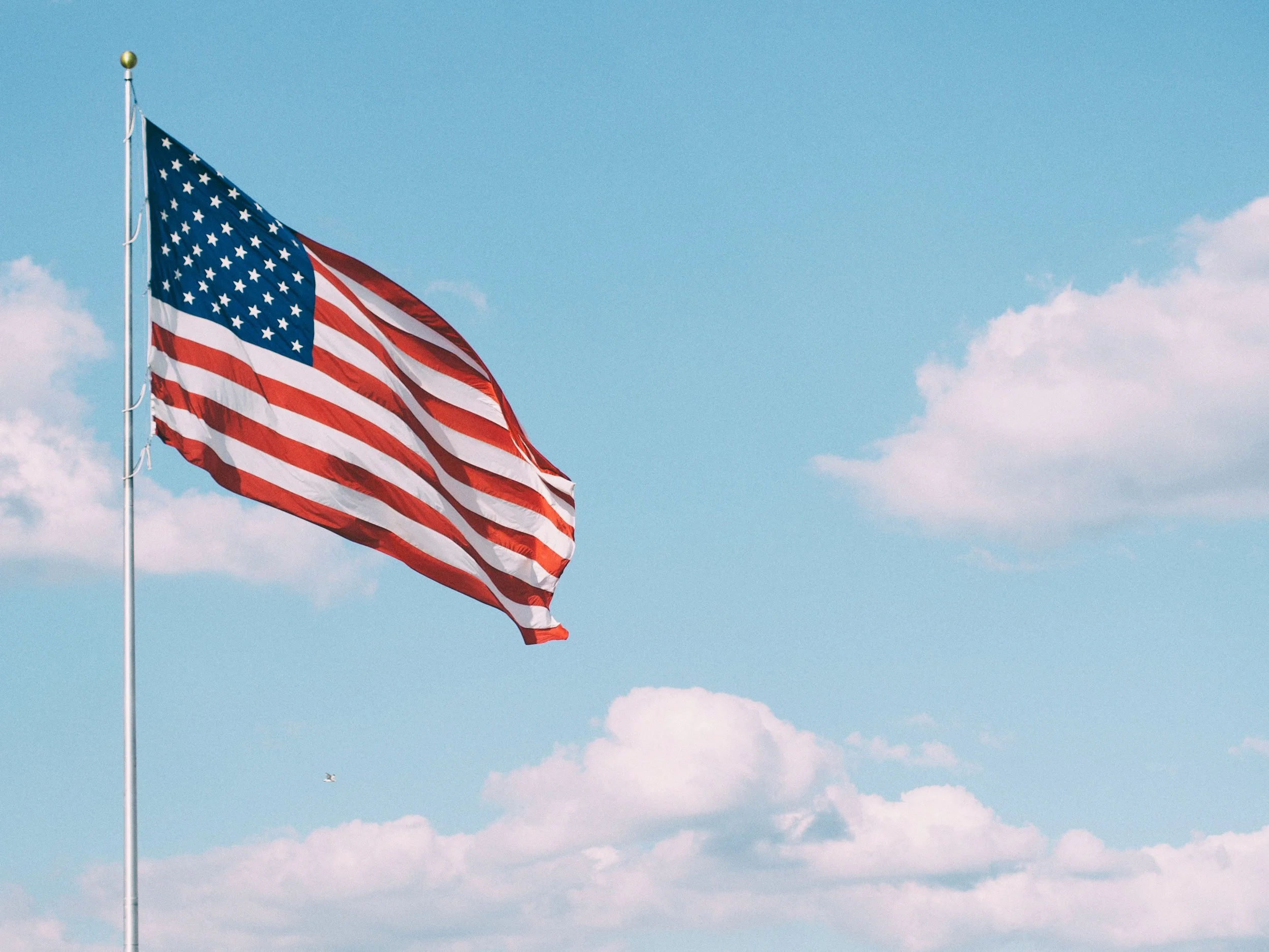 American flag waving in the wind against a blue sky with scattered clouds.