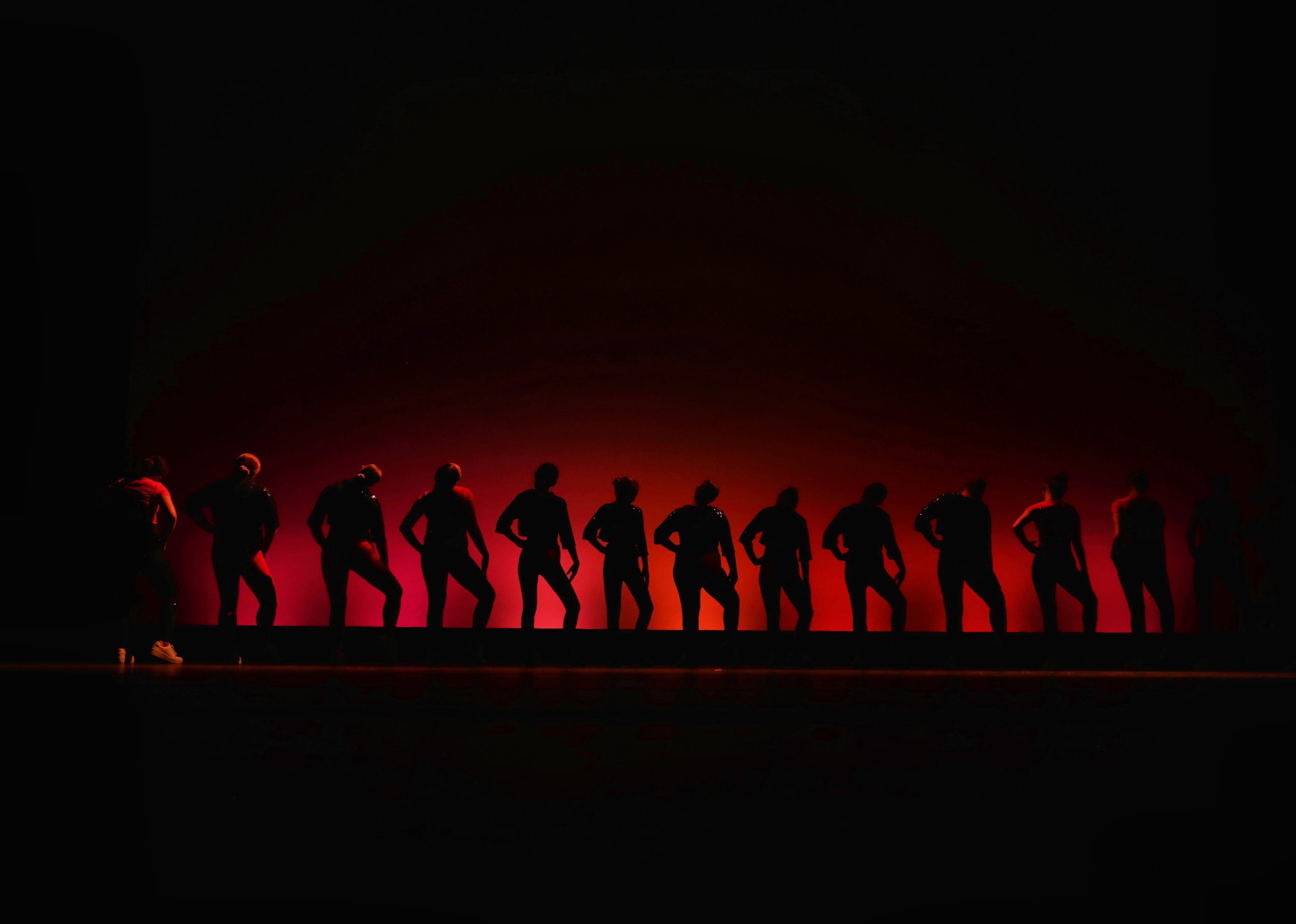 Silhouettes of dancers on stage against a red light background.