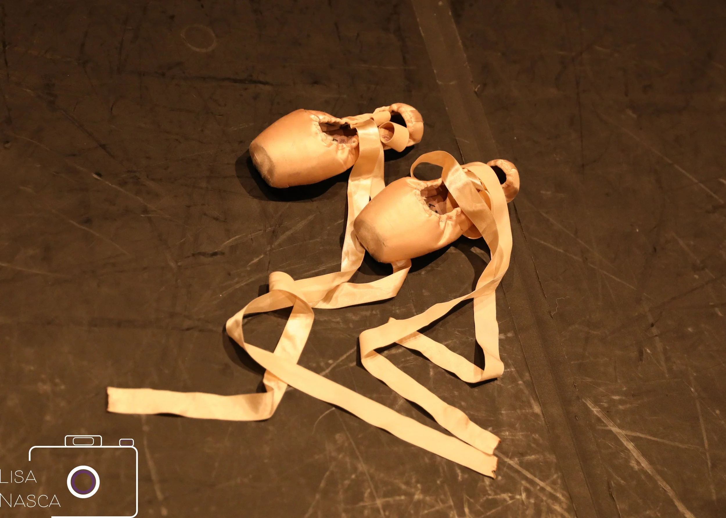 Pair of ballet slippers with ribbons on a dark floor.