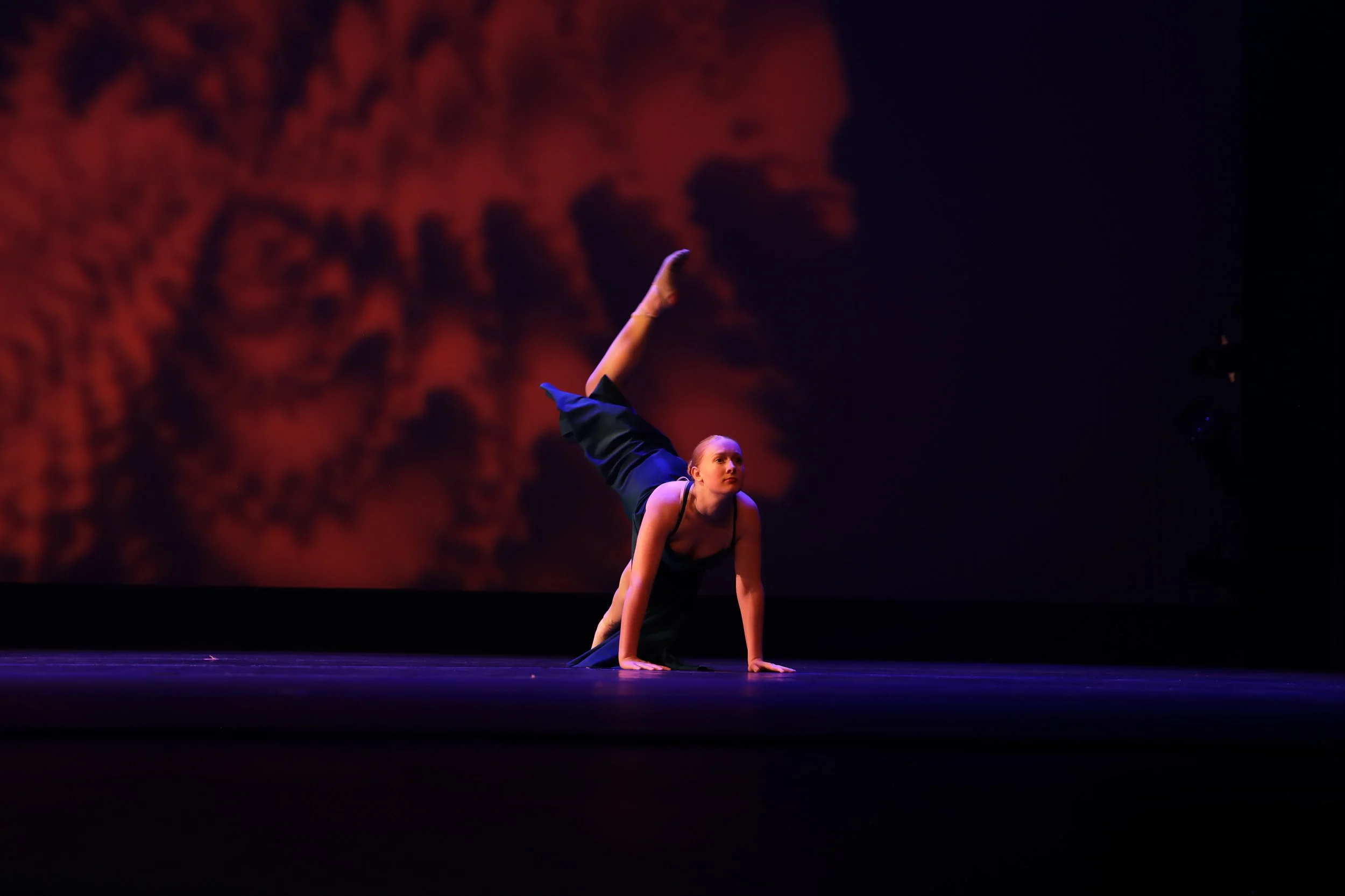 A female dancer performing a balancing move on stage with a dark, abstract background.