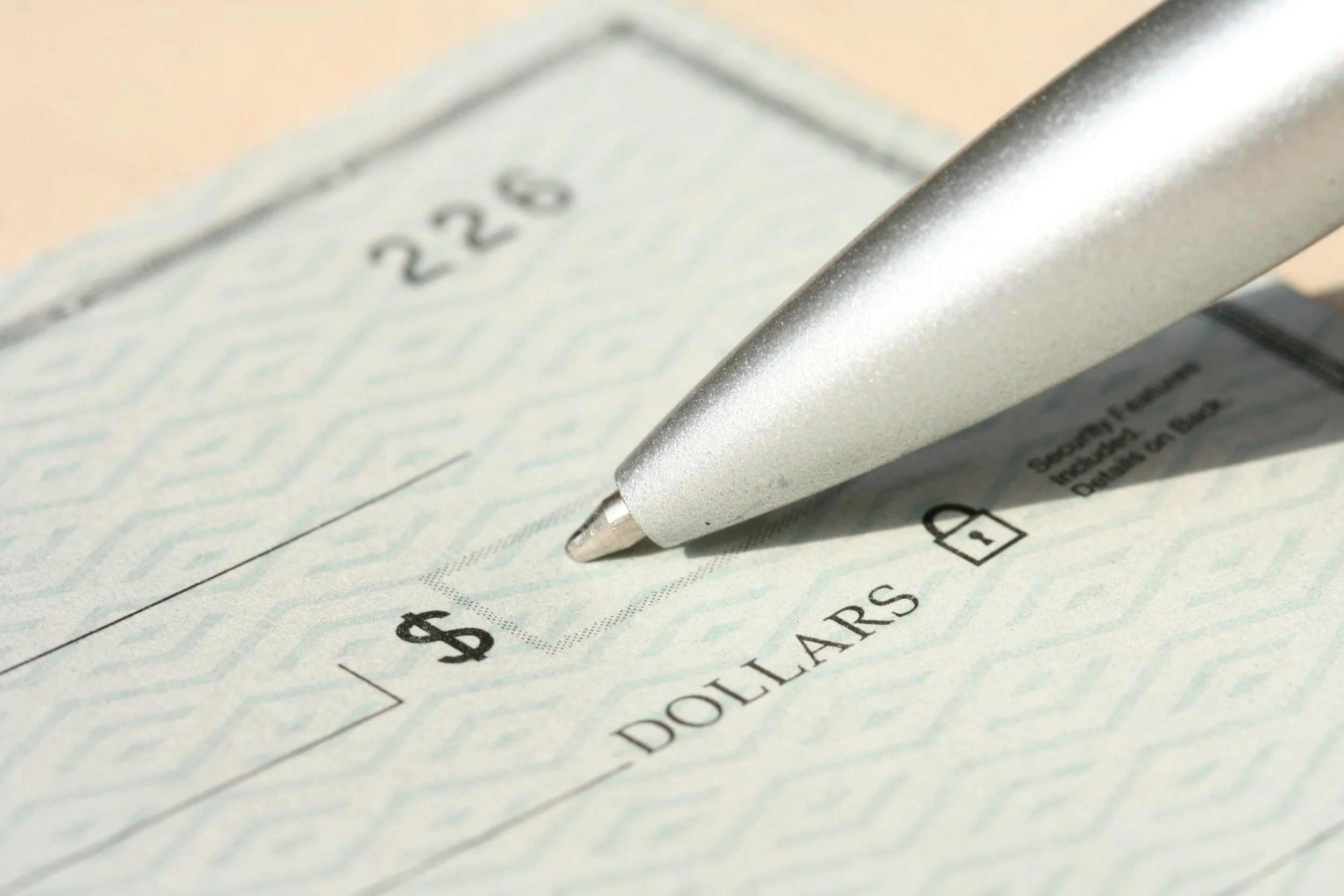 Close-up of a silver pen resting on a check with a $ in the amount box and a dotted line for the signature.