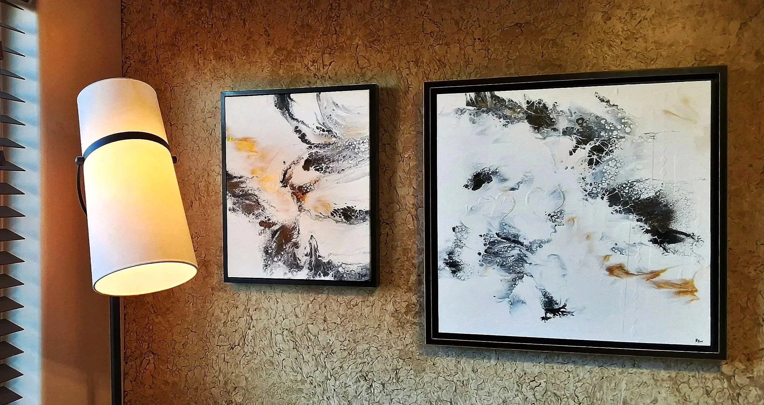 Decorative abstract black, white, and yellow paintings on a textured beige wall, with a standing lamp on the left side.