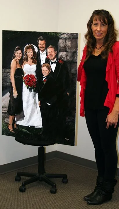 A woman stands next to a large family portrait on an easel in a room with plain white walls.