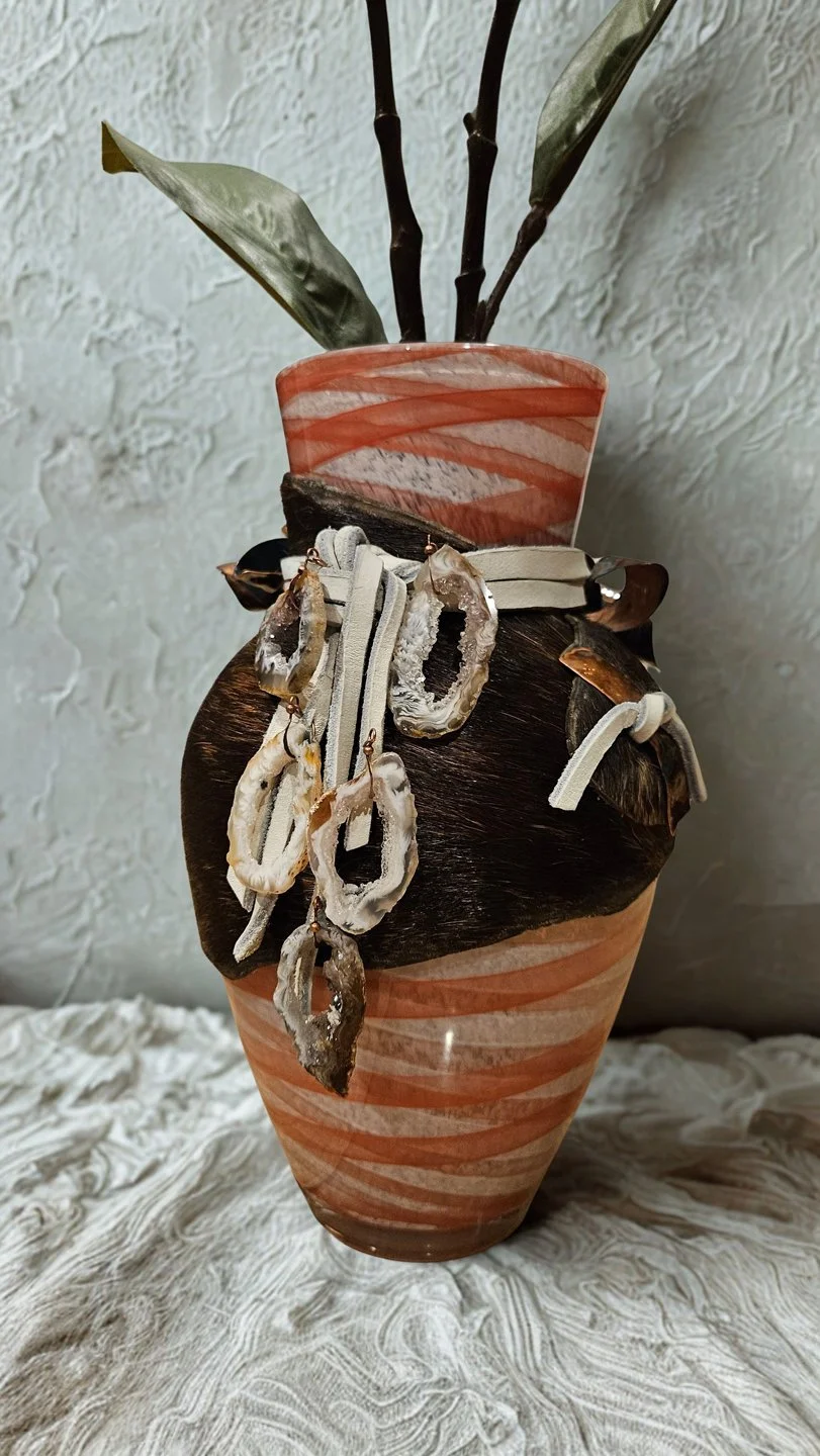 Decorative ceramic vase with green leaves and dried plant accents inside, placed on textured fabric surface.