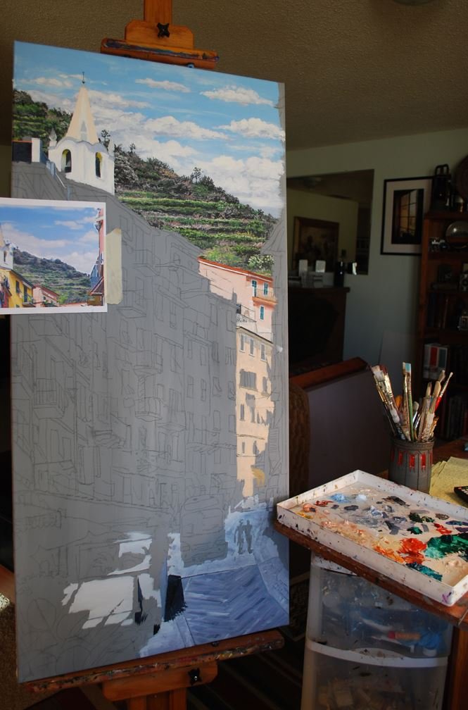 An artist is painting a scenic landscape of a hillside town with a church with a white steeple on an easel. The painting is partially finished, with the sky and hillside developed, and the lower part of the painting still in sketch form.