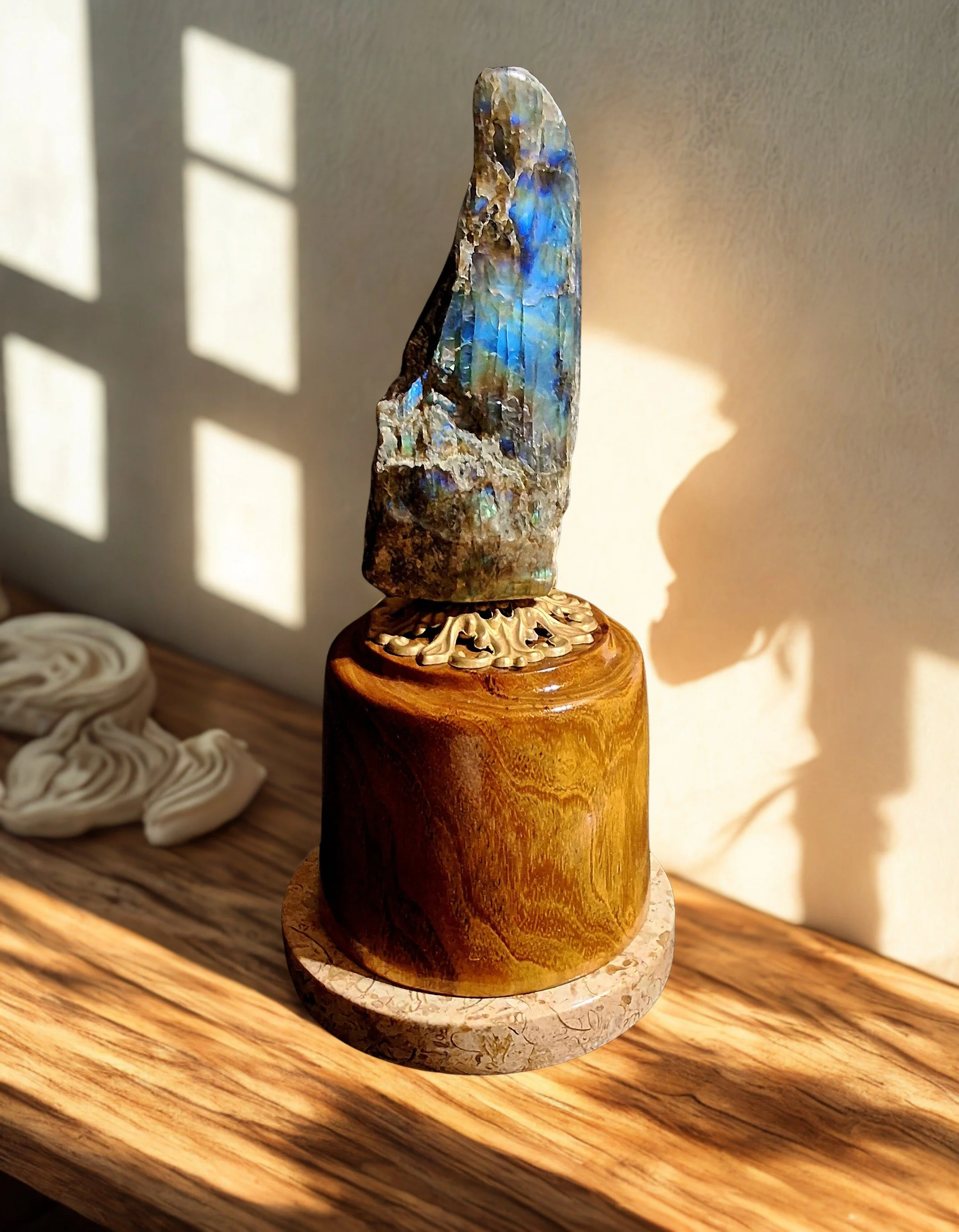 A decorative piece featuring an iridescent mineral or gemstone mounted on a wooden base, placed on a wooden surface with sunlight casting shadows.