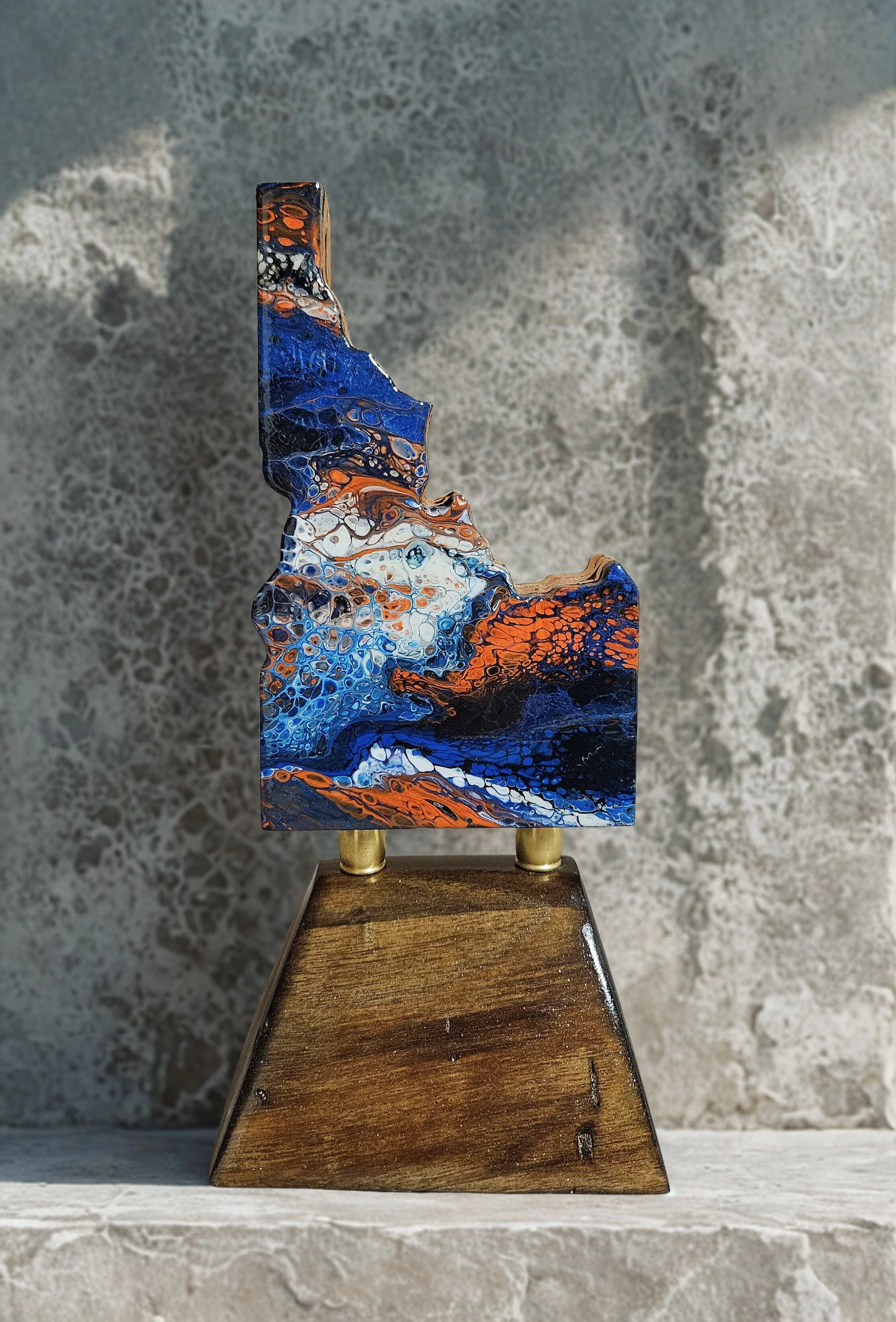 Abstract art sculpture with swirling blue, orange, white, and black colors, mounted on a wooden stand.