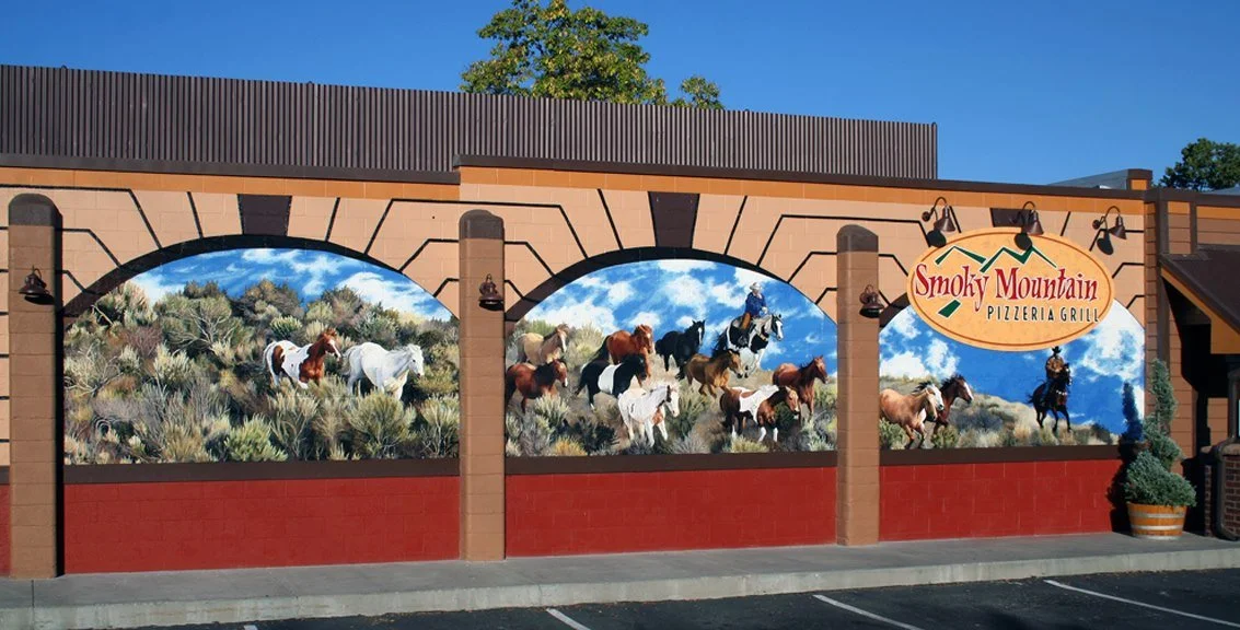 An exterior mural on a restaurant wall depicting wild horses in a desert landscape, with a sign reading "Smoky Mountain Pizzeria Grill."