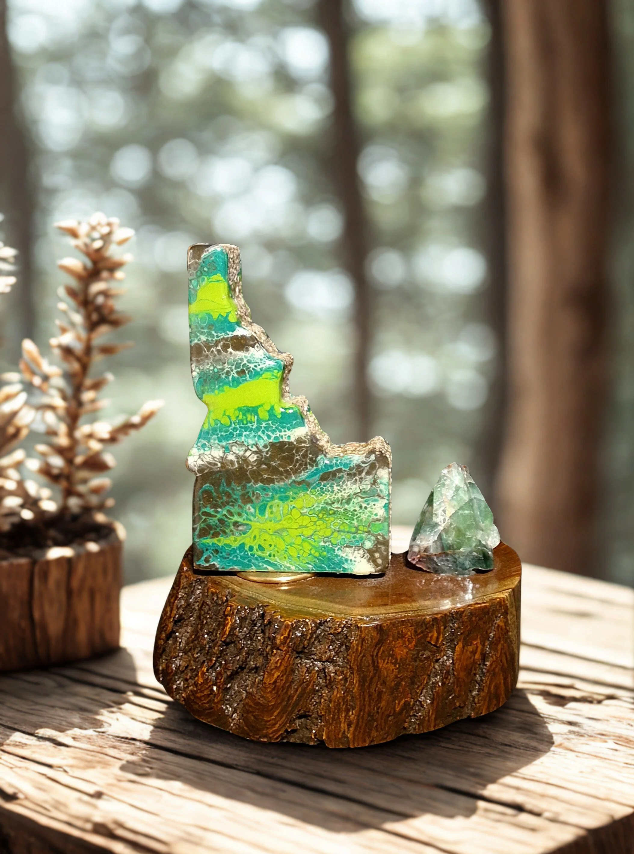 Colorful glass sculptures resembling a mountain and a crystal on a wooden base, with a pine cone in a wooden container in the background.