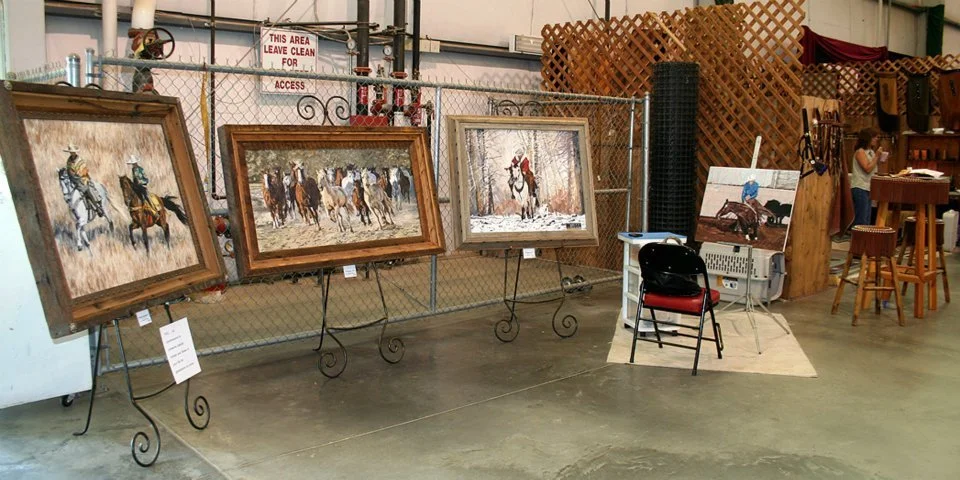 Paintings of horses on display in an art gallery or store, with a woman in the background observing artwork.