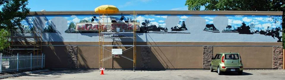A mural painting is being restored on a building wall, with scaffolding set up in front and a van parked nearby.