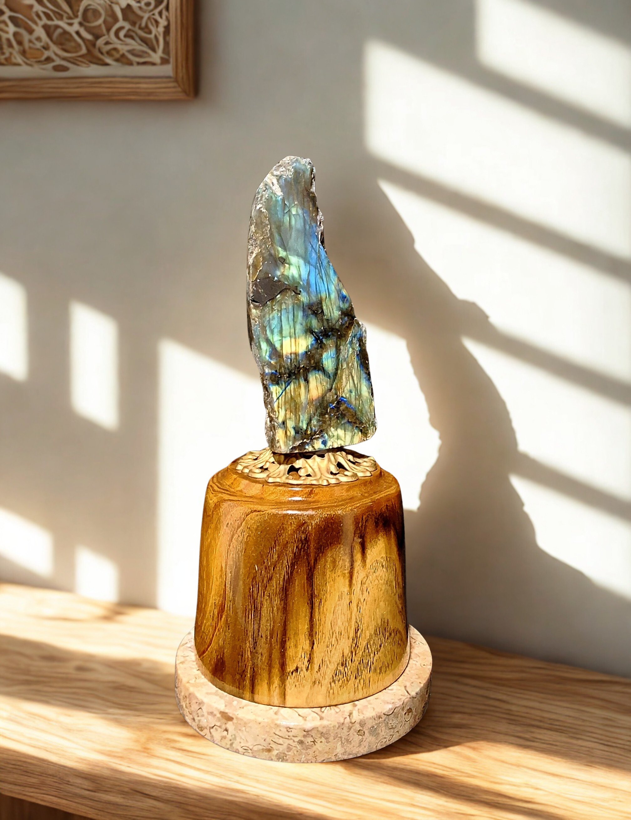 A decorative sculpture consisting of a colorful abalone shell mounted on a carved wooden stand, placed on a wooden surface with shadows cast on the wall behind.