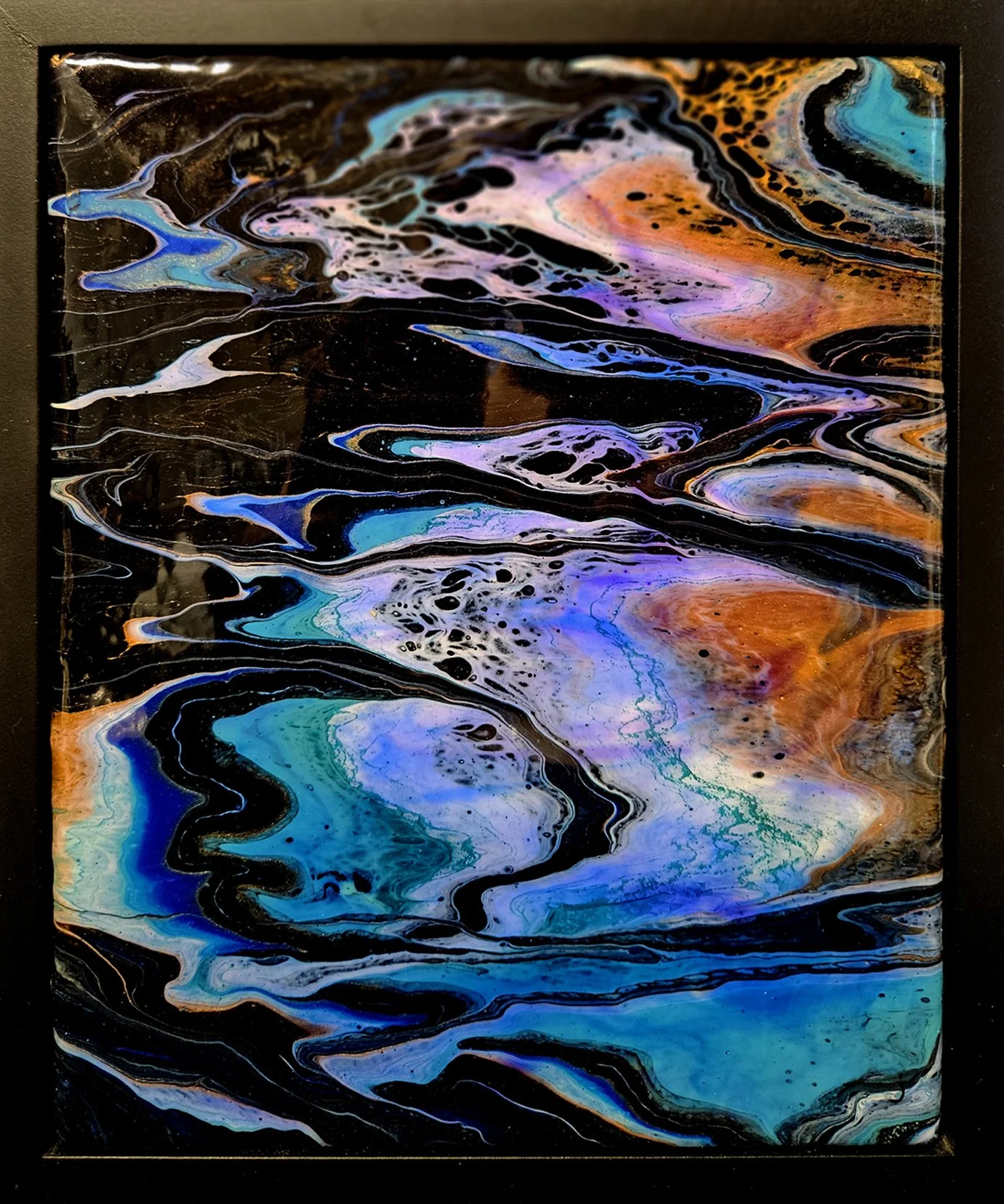 Abstract acrylic pouring artwork with swirling shades of blue, purple, orange, black, and hints of turquoise and pink framed in black.