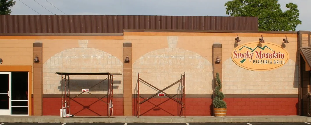 Exterior of Smoky Mountain Pizzeria Grill with entrance and window, outdoor scaffolding, and a potted plant