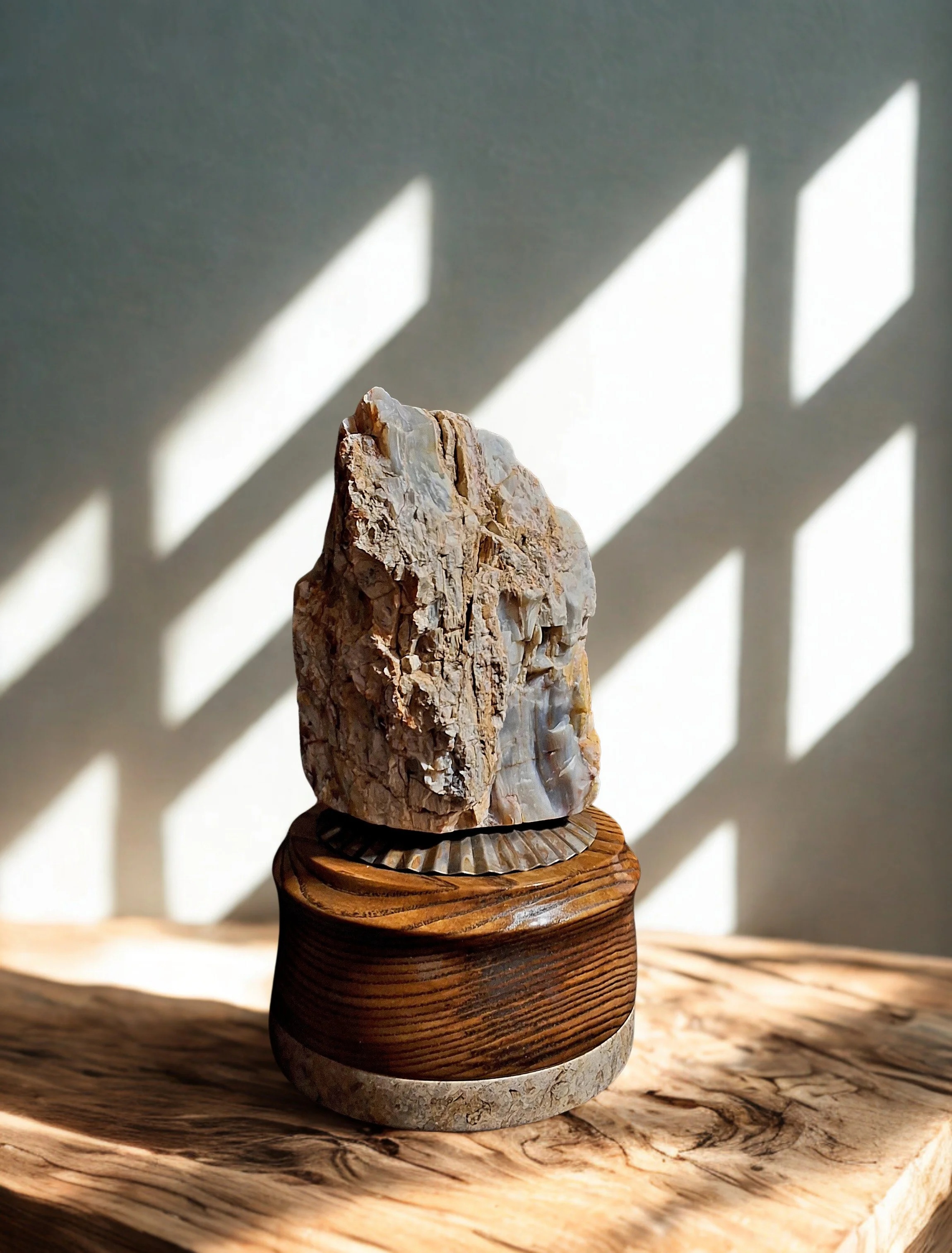 A piece of rough, textured stone or mineral on a carved wooden stand, with shadows of a window panes cast on the wall behind.