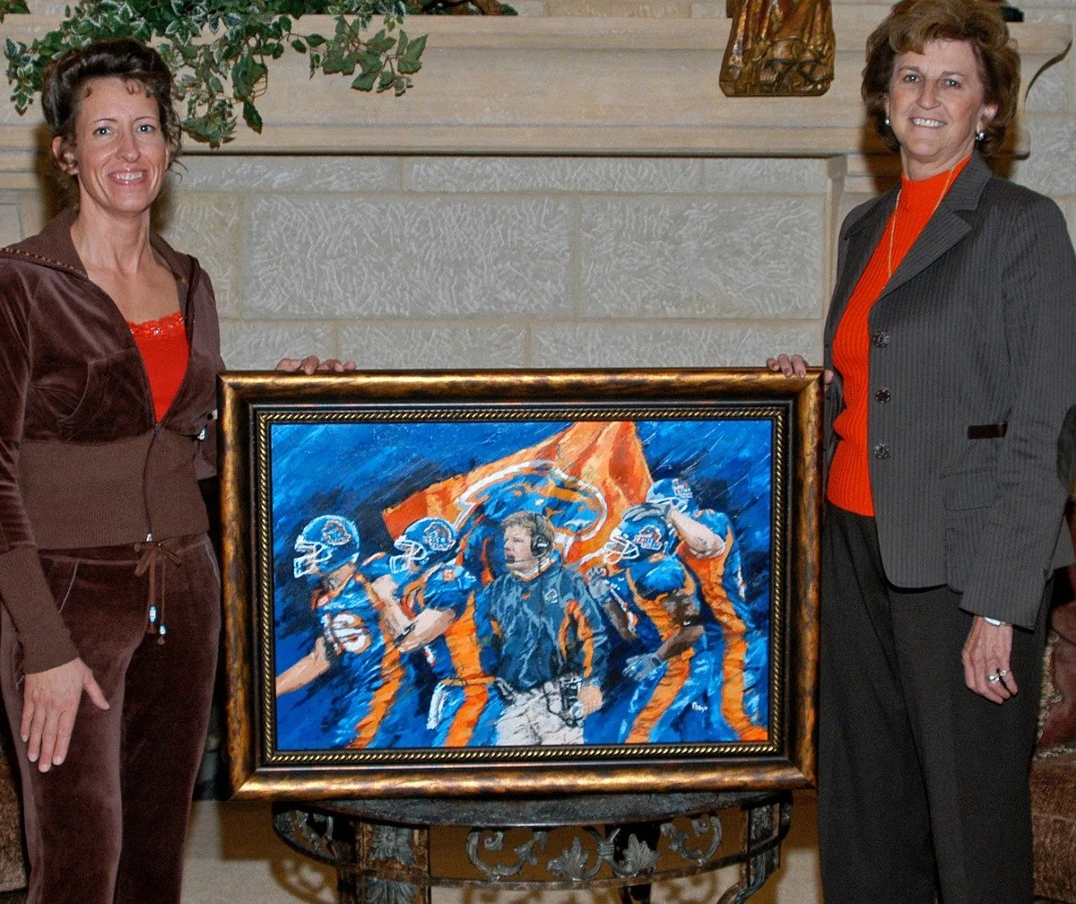 Two women standing on either side of a framed painting of a football team, with a coach or team leader in the center, resembling of a sports scene with players in uniform and a flag in the background.