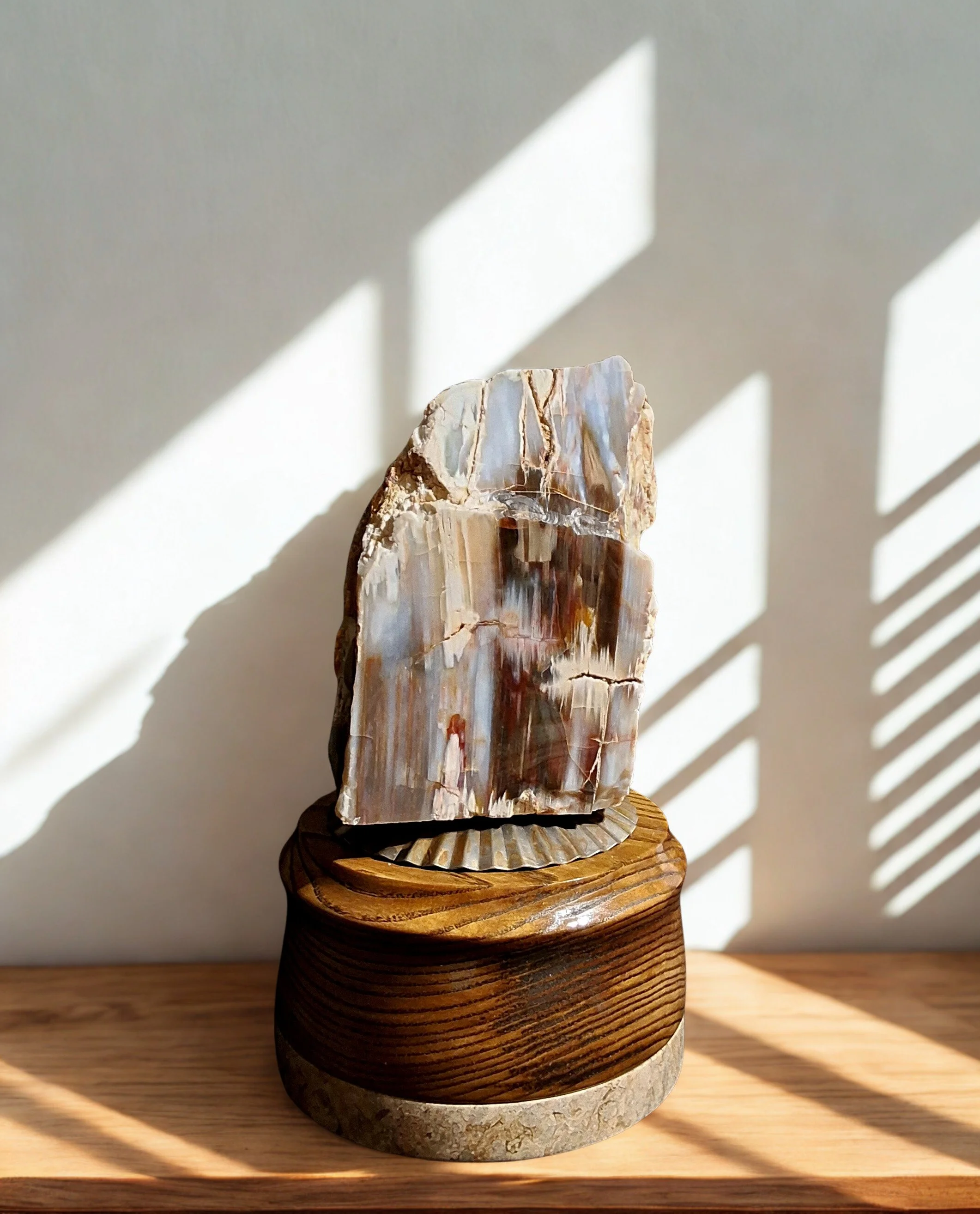 A decorative stone sculpture placed on a wooden stand, with sunlight casting shadows through window blinds.
