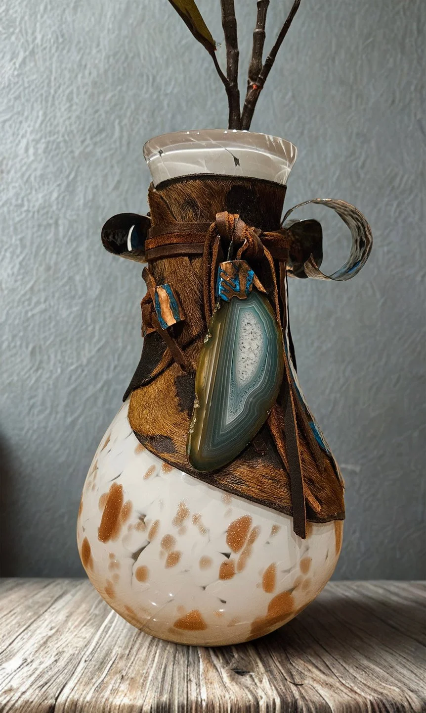 Ceramic vase with a textured white and brown pattern, decorated with brown leather and wooden ribbons, and an agate stone hanging on the front. There are also dark sticks or twigs in the vase.