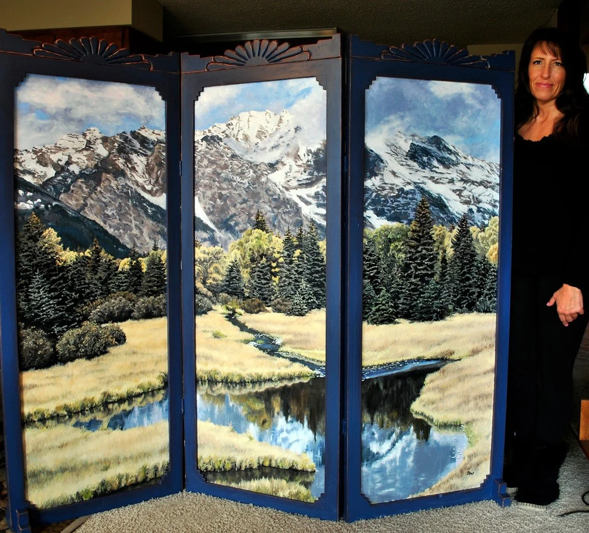 A three-panel painted screen depicts a scenic mountain landscape with snow-capped peaks, green pine trees, and a meandering stream reflecting the sky, with a woman standing beside it.